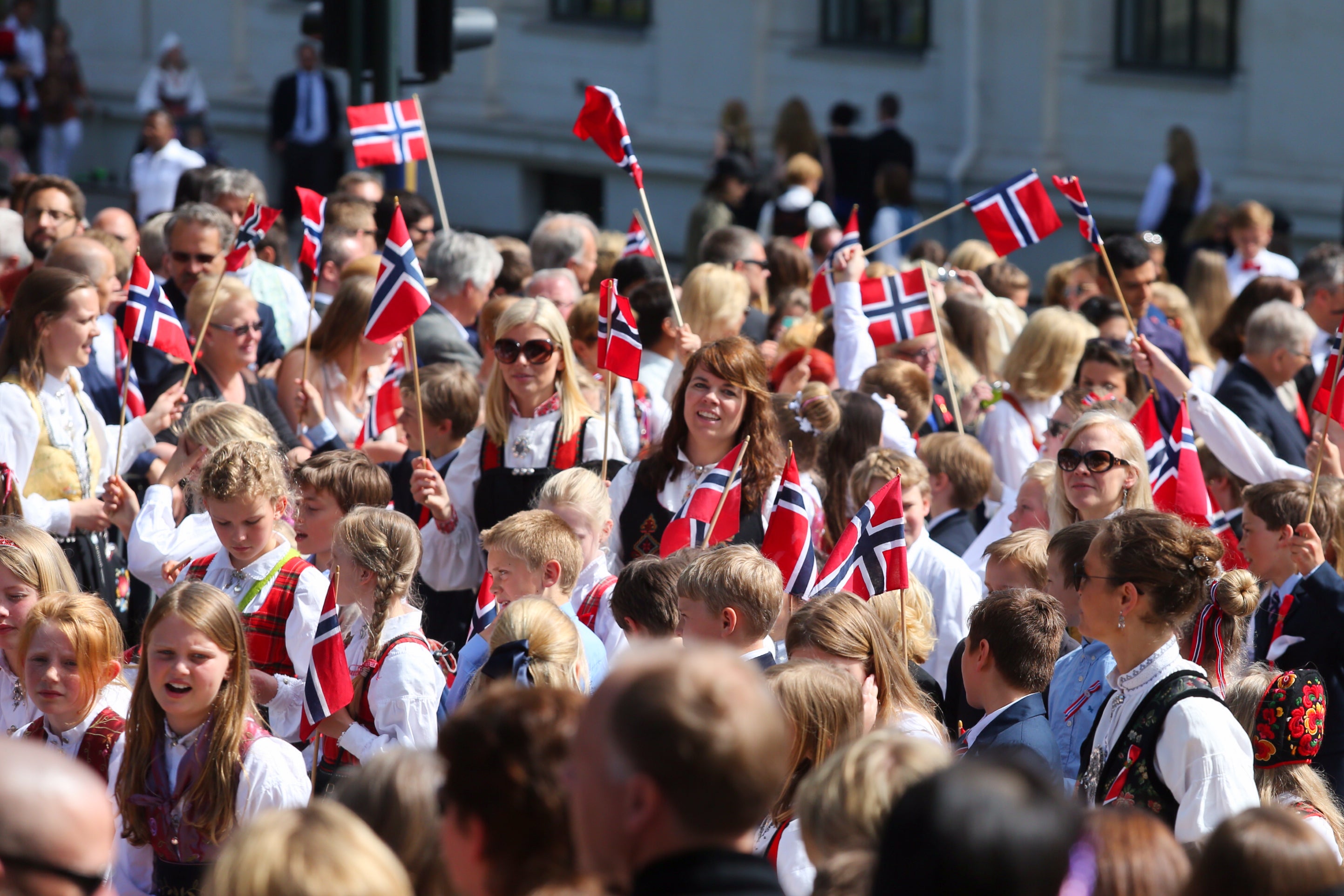 En folksamling med många människor som håller norska flaggor under en utomhusceremoni.