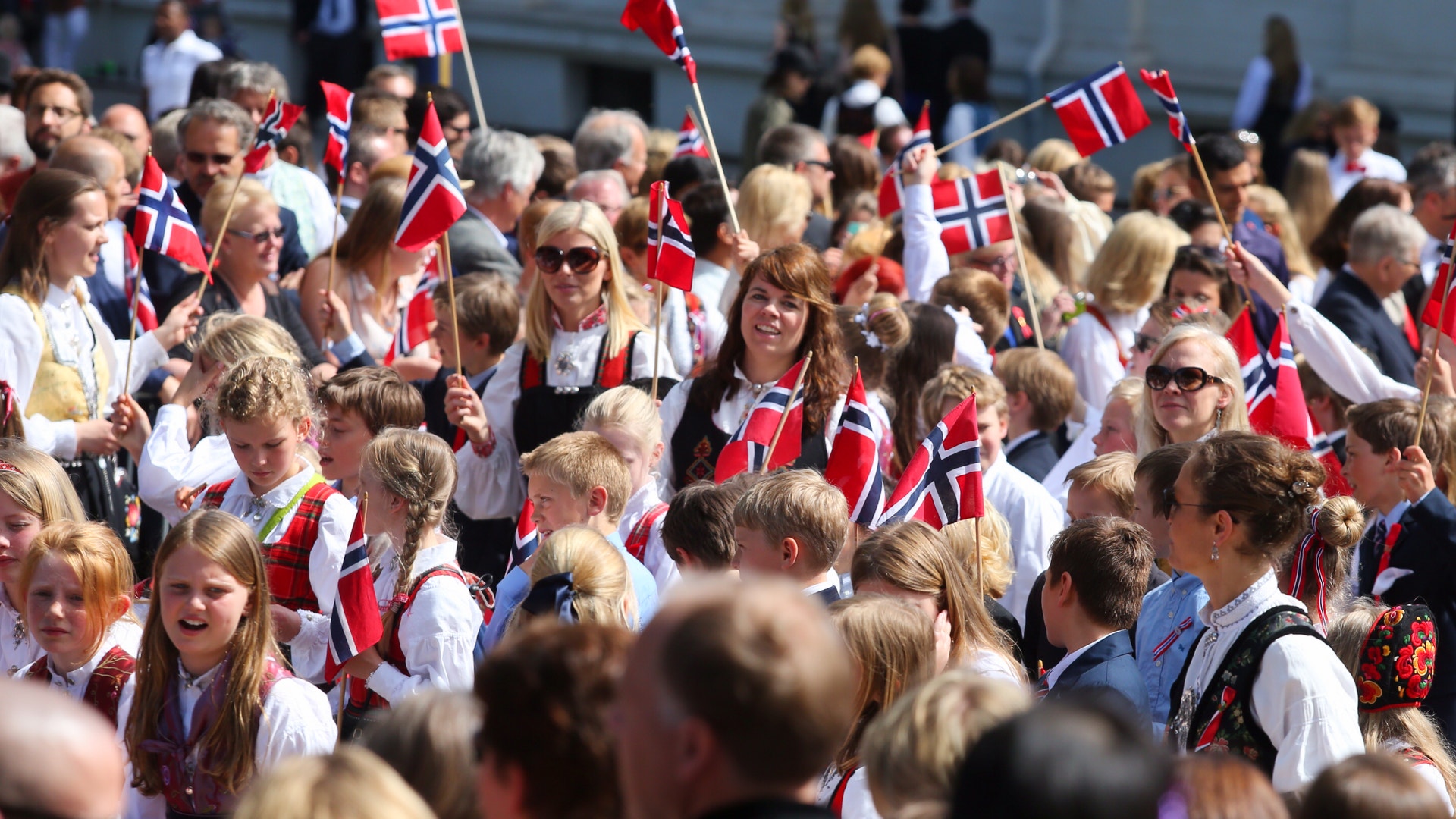 En folksamling med många människor som håller norska flaggor under en utomhusceremoni.