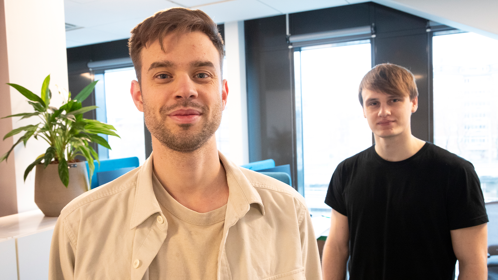 Två män i ett modernt kontor med naturligt ljus och växter i bakgrunden.