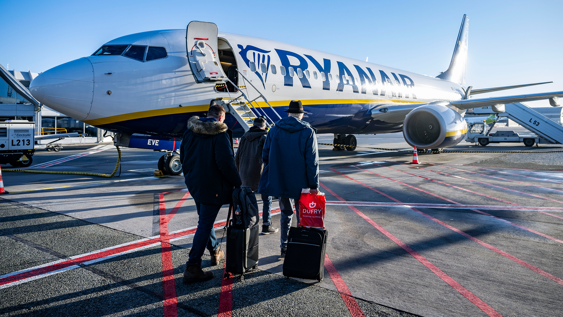 Ett blått och vitt Ryanair-flygplan på landningsplatsen med passagerare som går ombord via trappan.