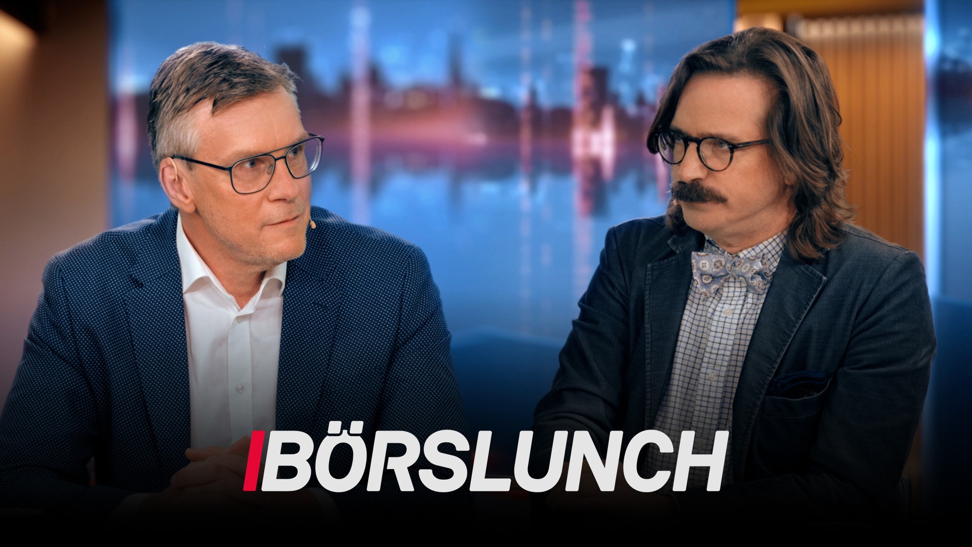 Två män i affärskläder sitter vid ett bord och diskuterar. I bakgrunden syns en stadshorisont. Texten Börslunch visas längst ned på skärmen.