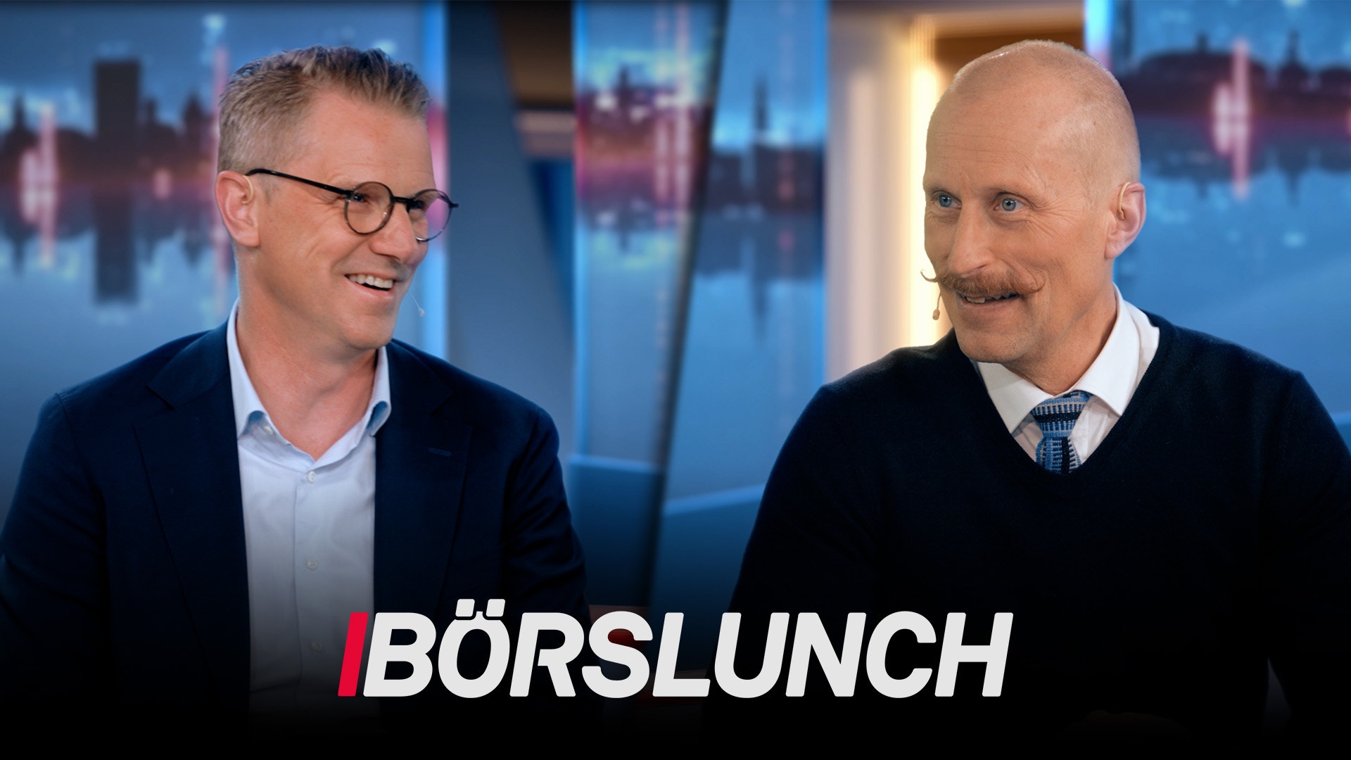 Två män i affärskläder diskuterar vid ett studio med stadsskyline i bakgrunden. Text visar 'BÖRSLUNCH'.