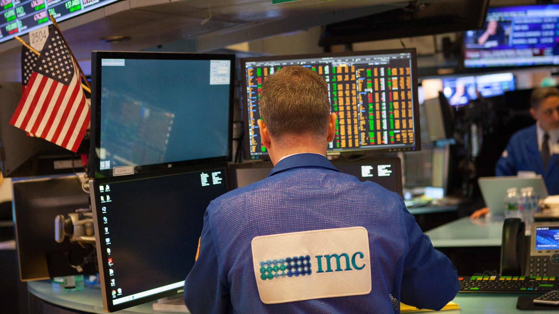 Handlare vid New York Stock Exchange sitter vid handelsskrivbord med flera skärmar som visar aktiemarknaddata