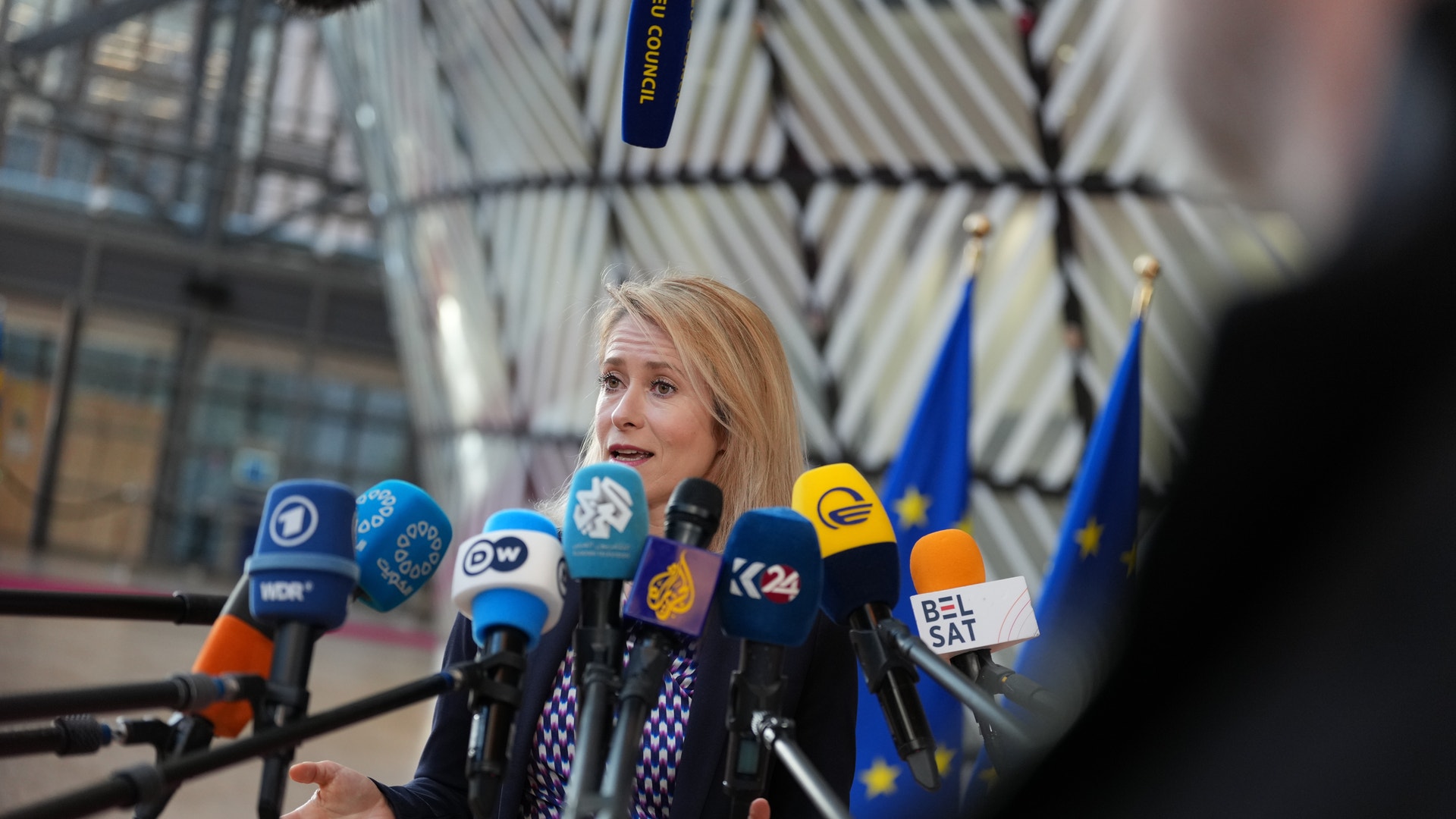 En kvinna ger ett uttalande vid en presskonferens omgiven av mikrofoner från olika nyhetsmedier.