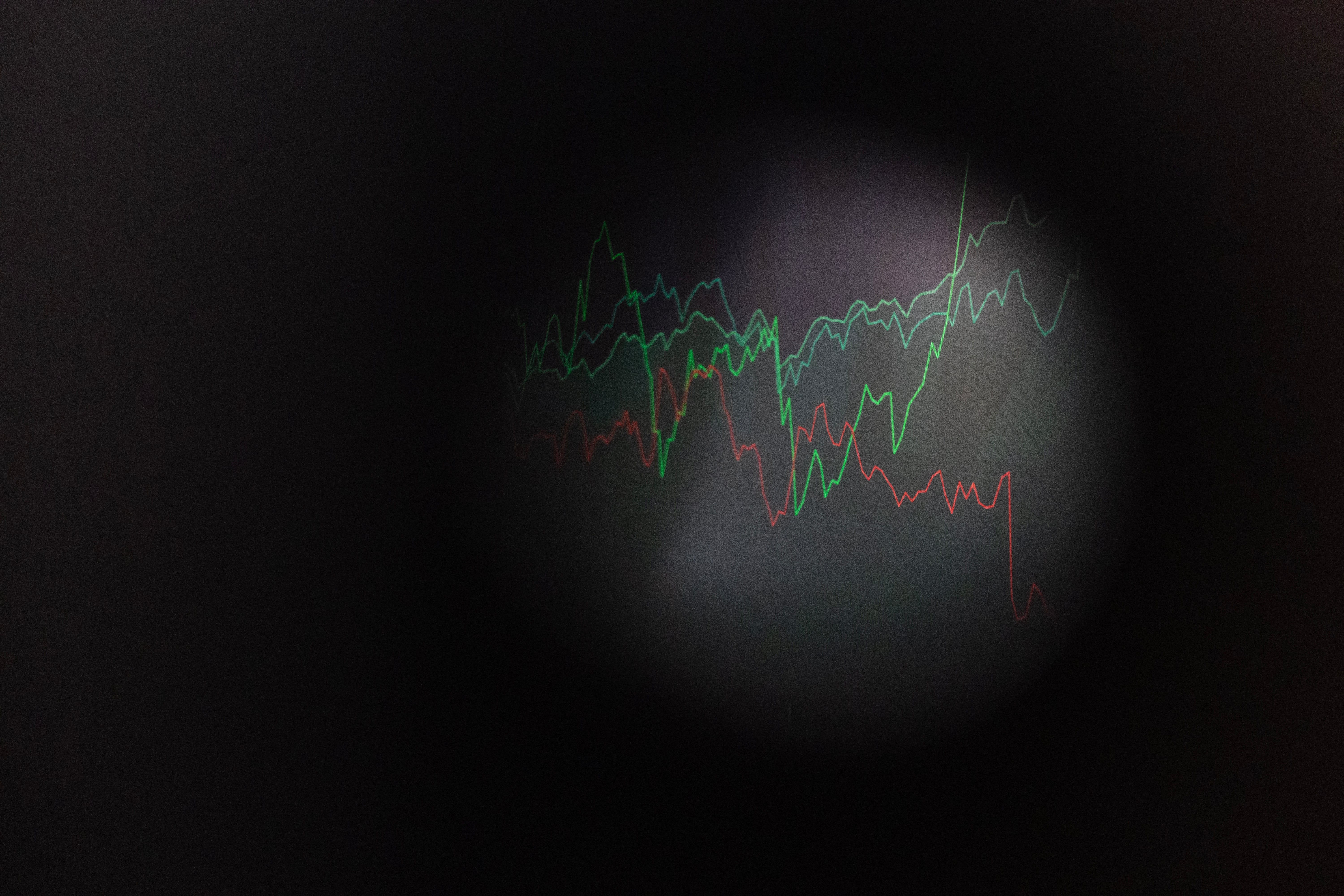 Grafisk illustration med flera färgade linjegrafer som visar trendlinjer mot en mörk bakgrund. De gröna, röda och gula linjerna representerar olika dataserier eller utvecklingslinjer.