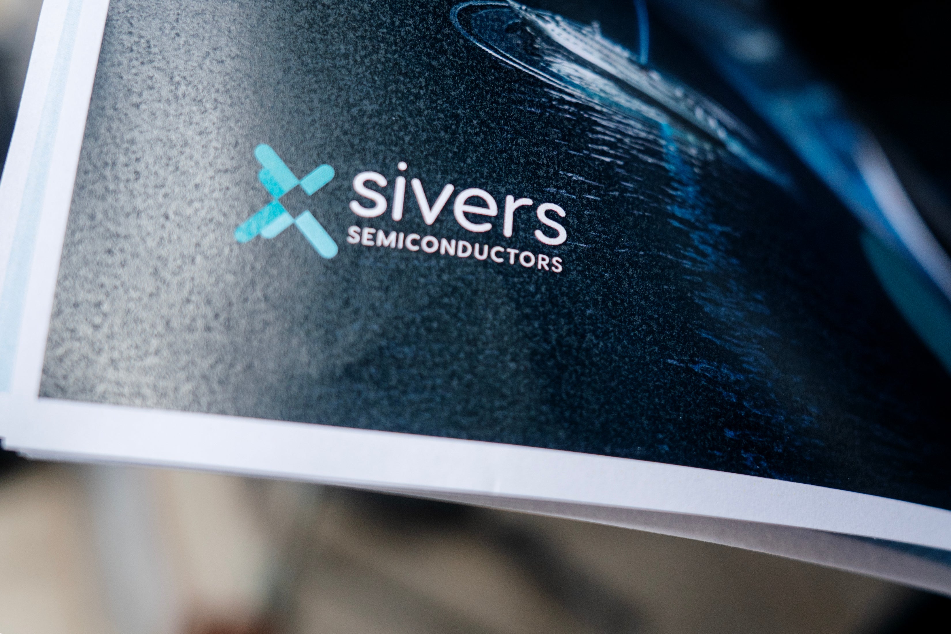 Skärm som visar Sivers Semiconductors logotyp med turkost X-symbol och företagsnamn på mörk bakgrund