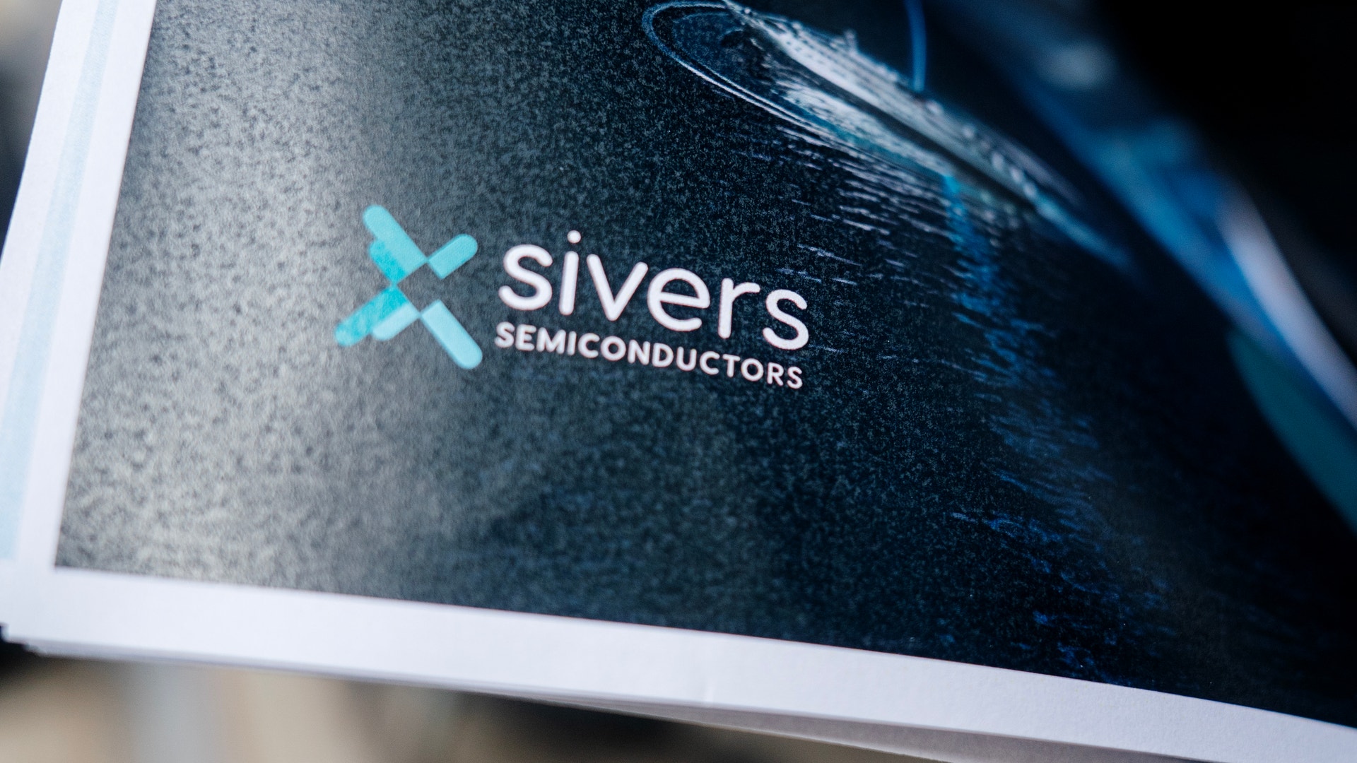 Skärm som visar Sivers Semiconductors logotyp med turkost X-symbol och företagsnamn på mörk bakgrund