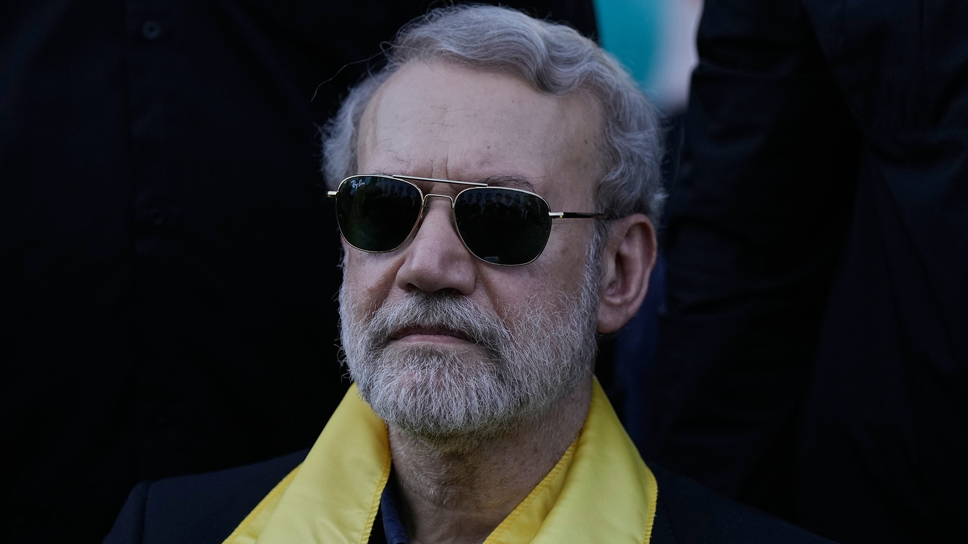 Porträtt av en man med solglasögon och gul kläder mot mörk bakgrund