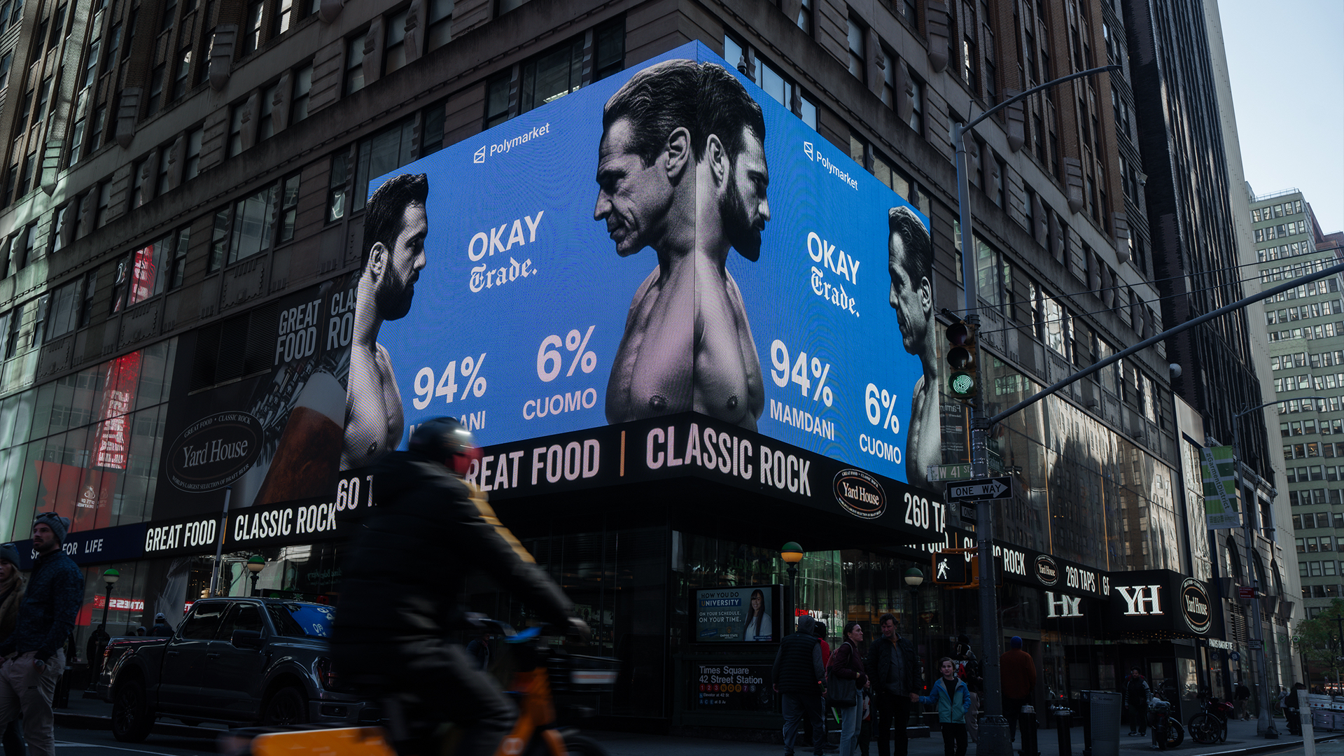 En stor digital skylt på en stadsfasad visar ansikten på människor med blå bakgrund och procentsatser.