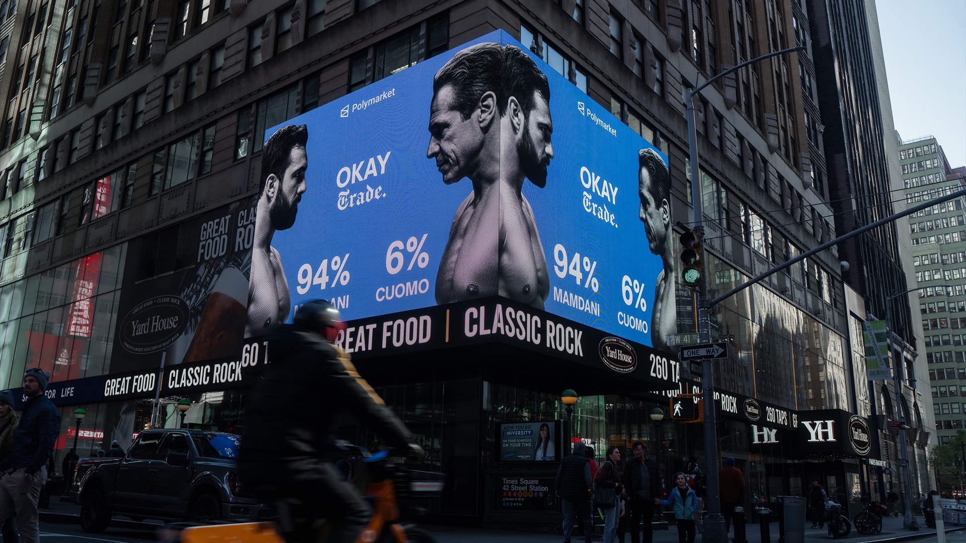 En stor digital skylt på en stadsfasad visar ansikten på människor med blå bakgrund och procentsatser.