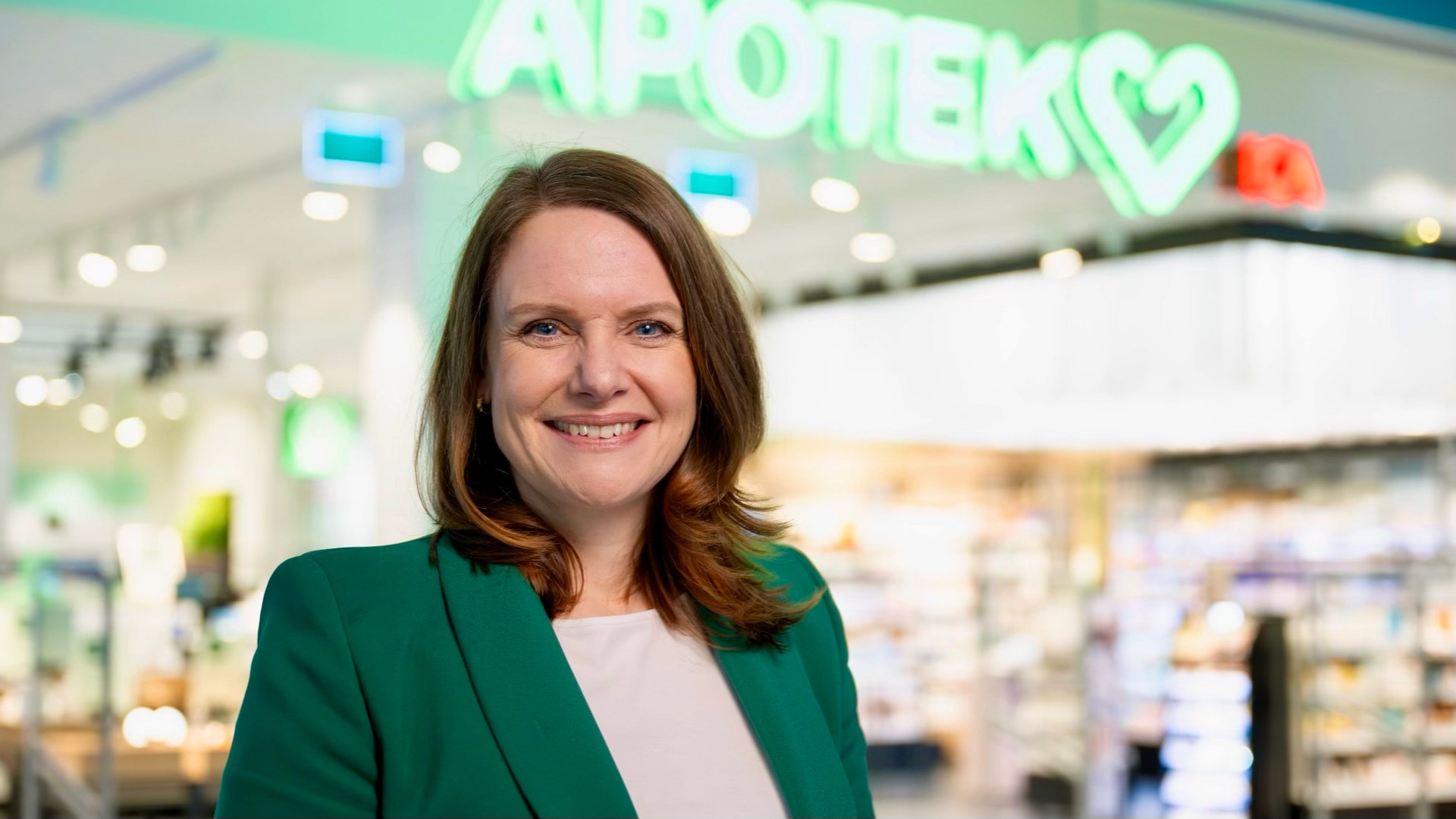 Porträtt av en kvinna i grön blazer framför ett apotek