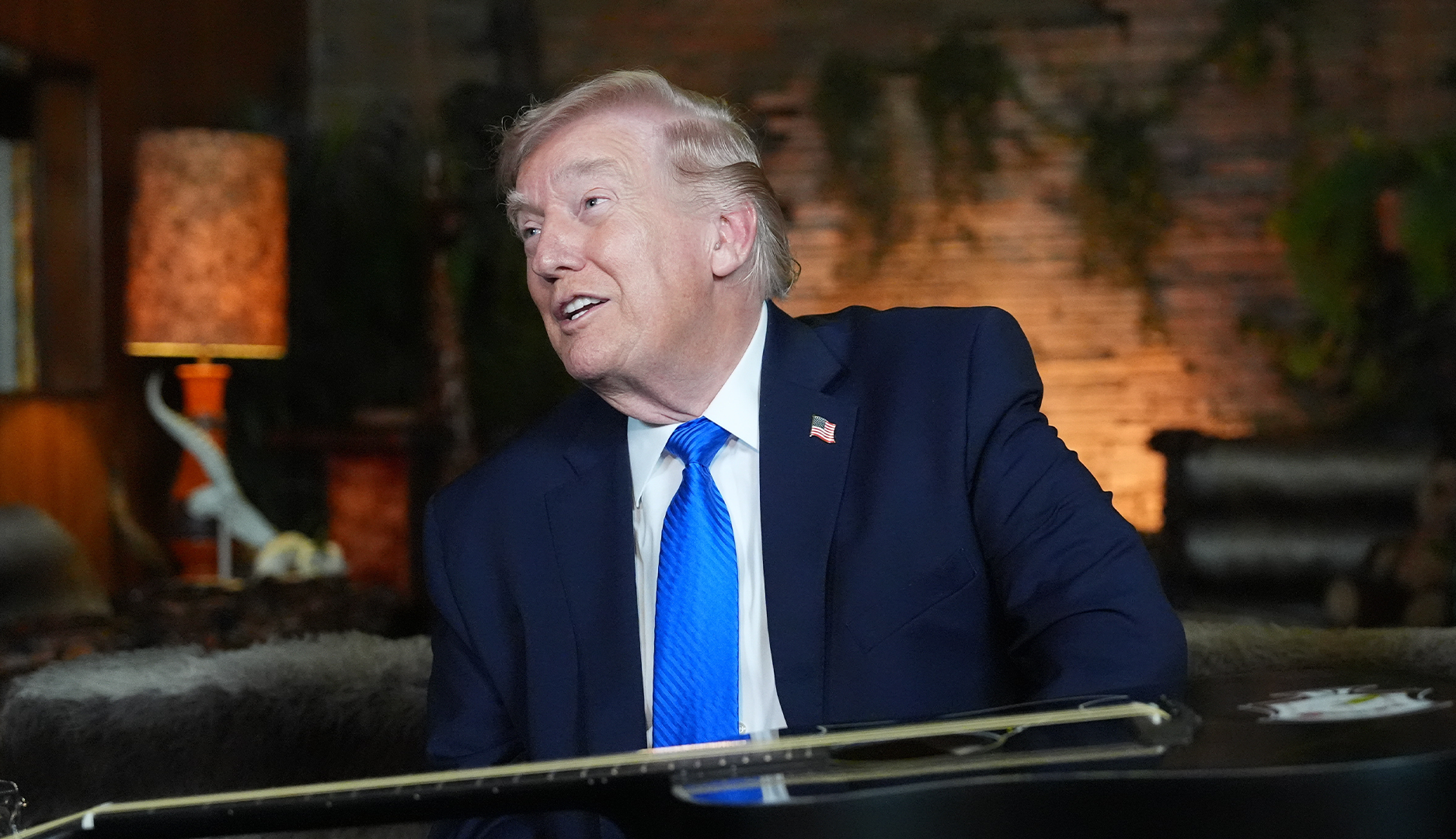 Porträtt av man i mörk kostym och blå slips i en inomhusmiljö med varm belysning.