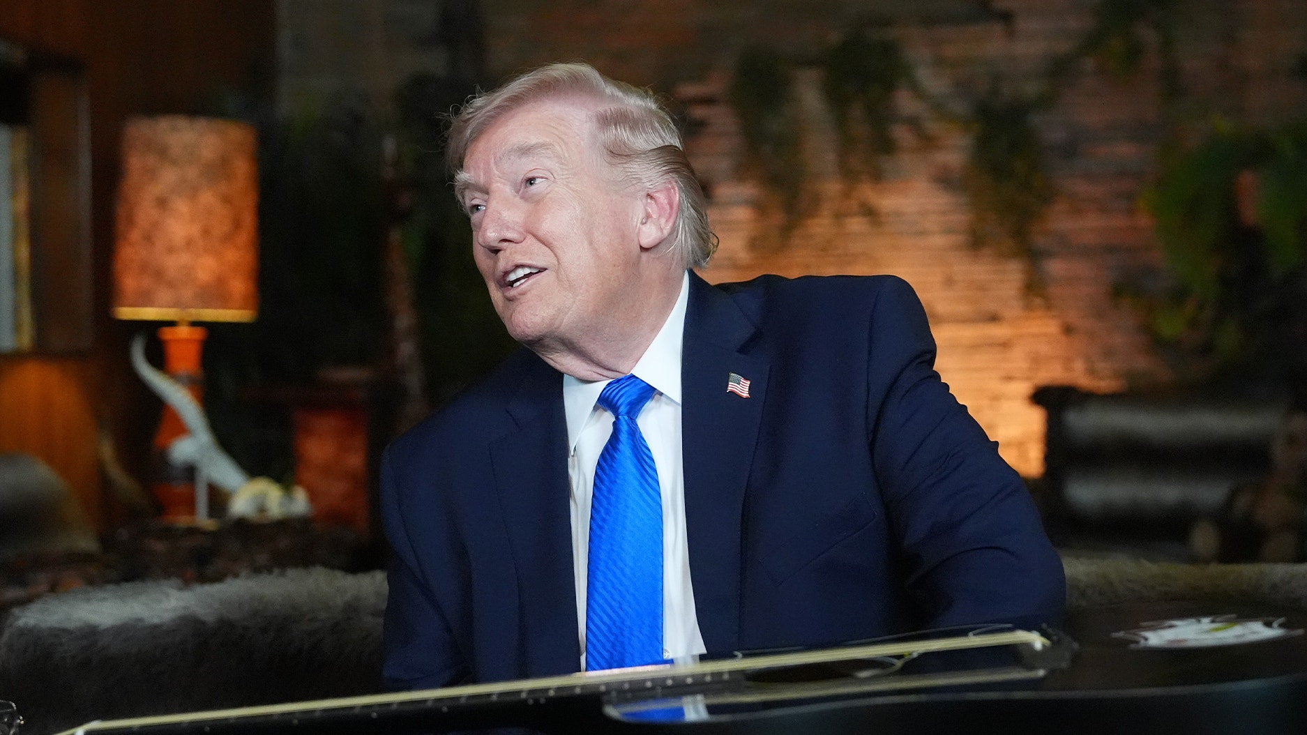 Porträtt av man i mörk kostym och blå slips i en inomhusmiljö med varm belysning.