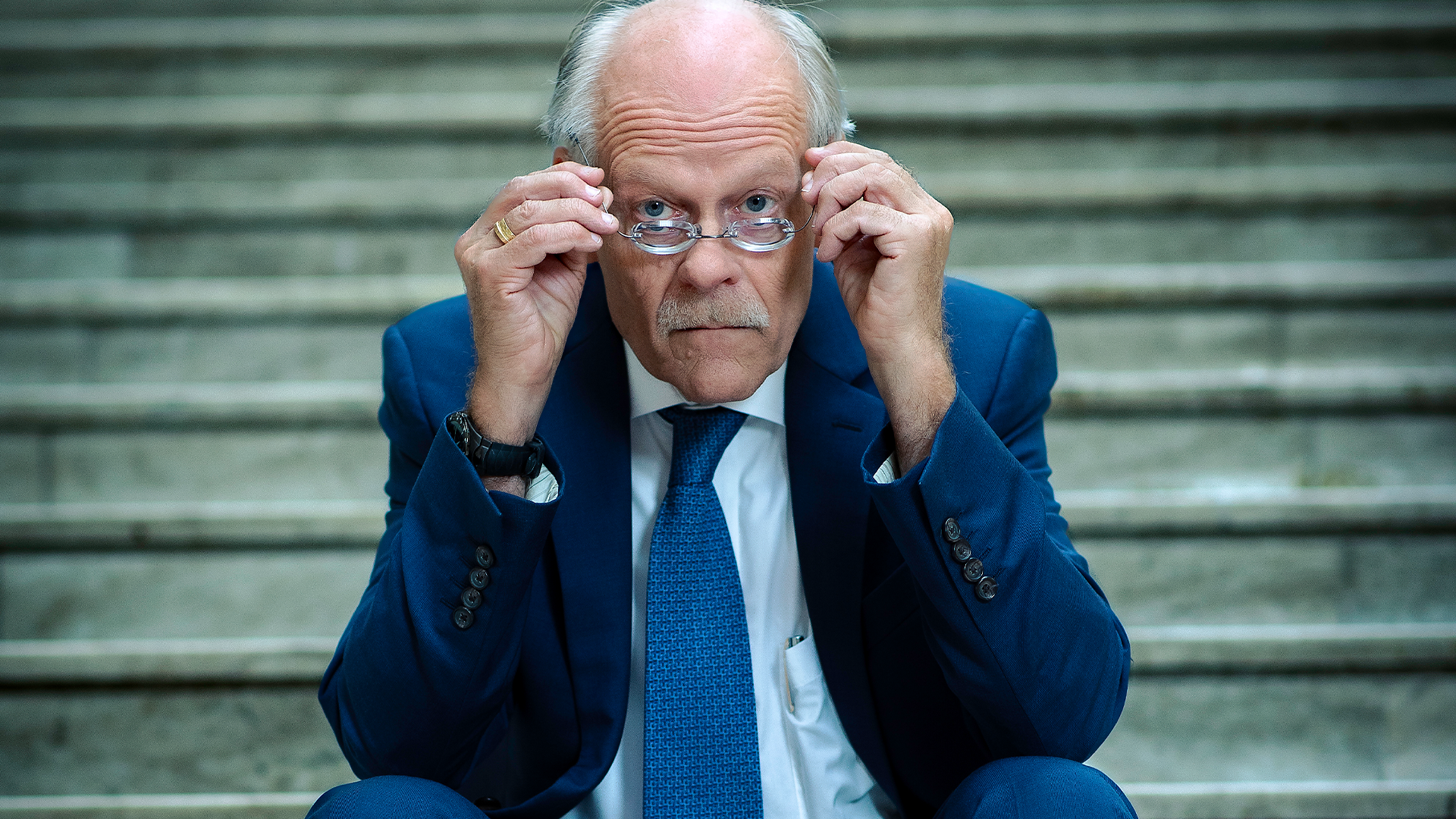 Stefan Ingves tittar fram över sina glasögon. Han sitter på en trappa.