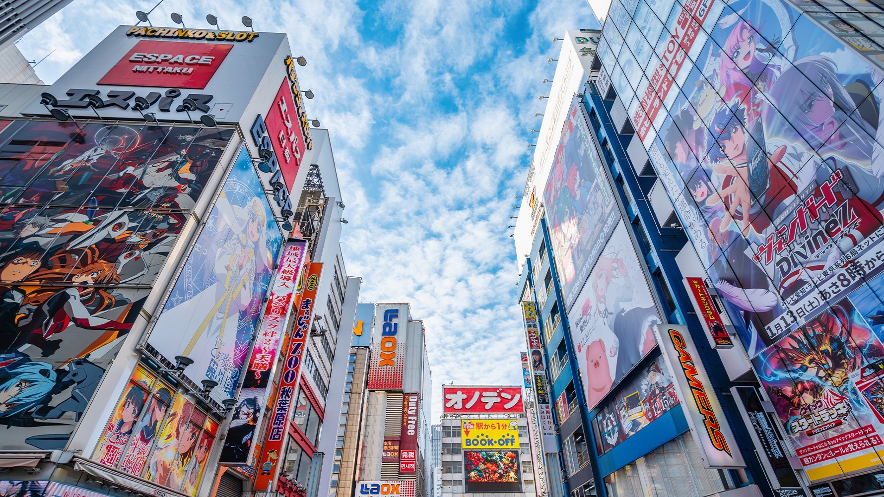 Japansk stadsgata med höga byggnader täckta av färgglada reklamskyltar och neonskyltar under blå himmel.