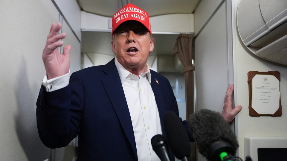 Donald Trump håller ett tal till reportrar på flyget Air Force One. Han är på sig röd keps och mörkblå kavaj.