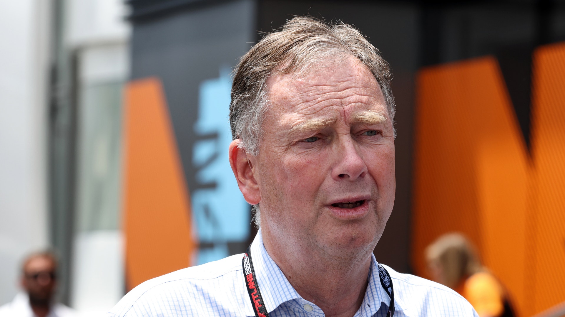 En man i ljusblå skjorta talar utomhus framför en orange byggnad.