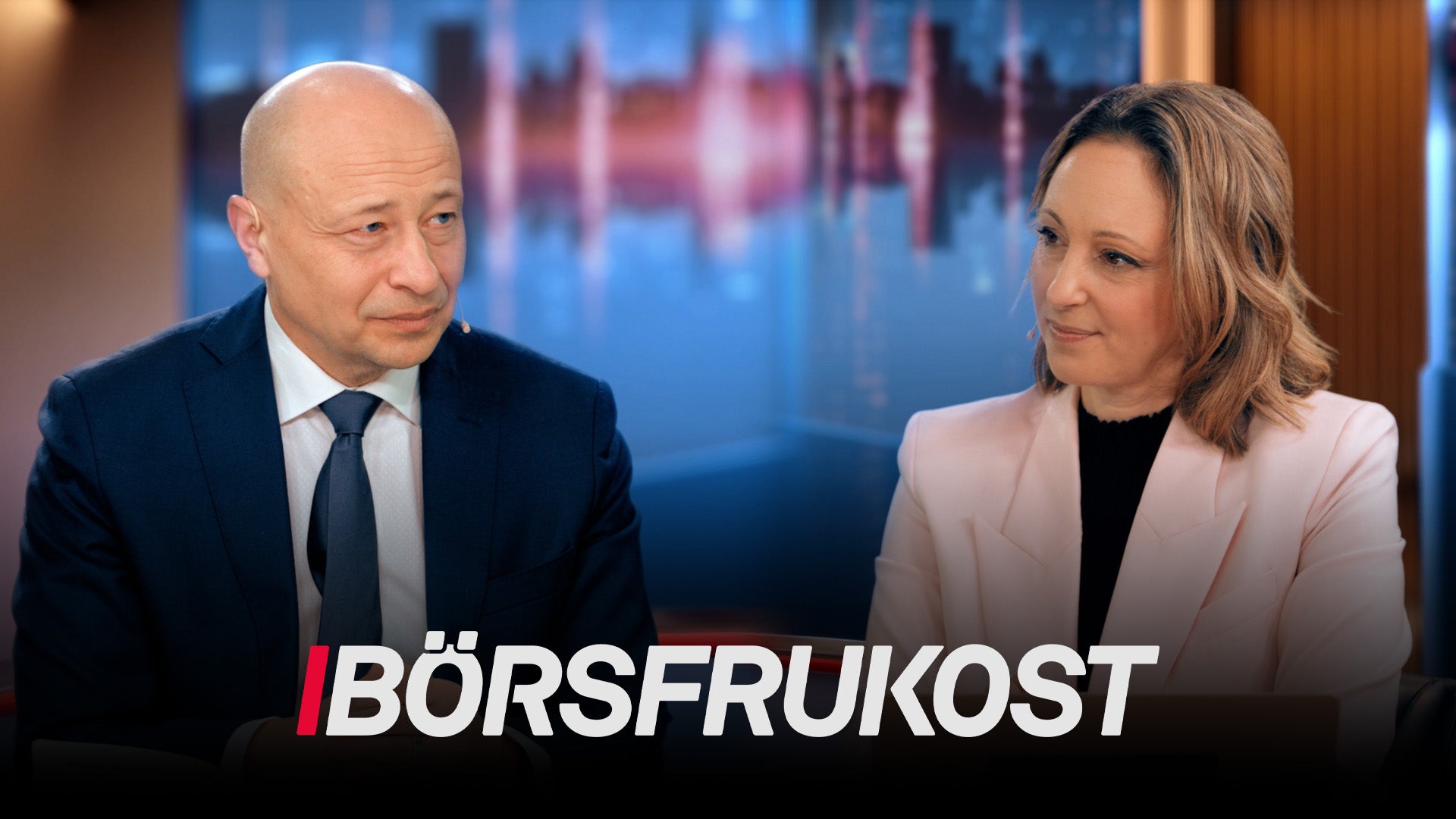 Två personer i affärskläder sitter framför en stadshorisont under texten Börsfrukost