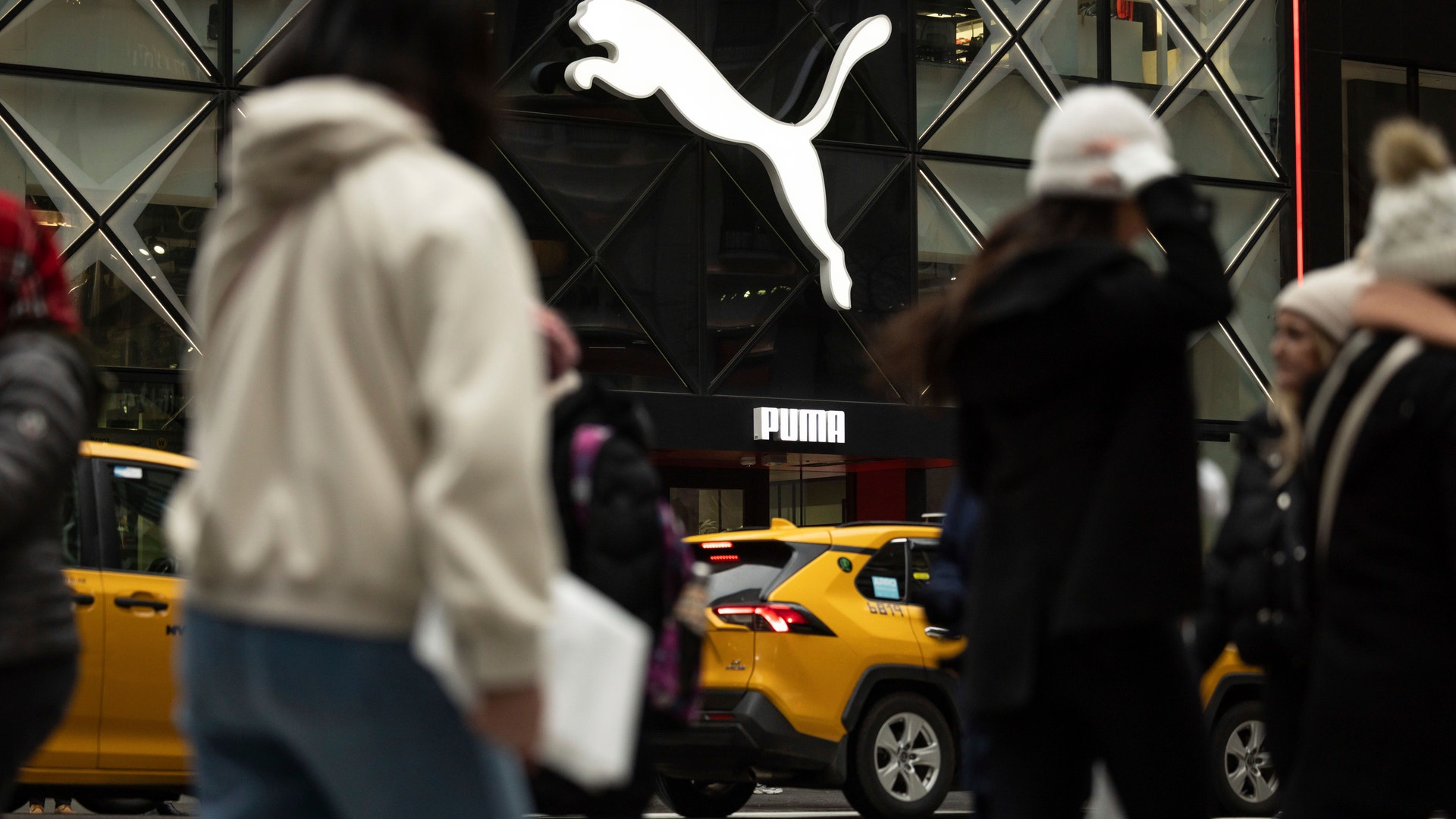 Puma-butiks skyltfönster på en stadsgata med fotgängare och gula taxibilar