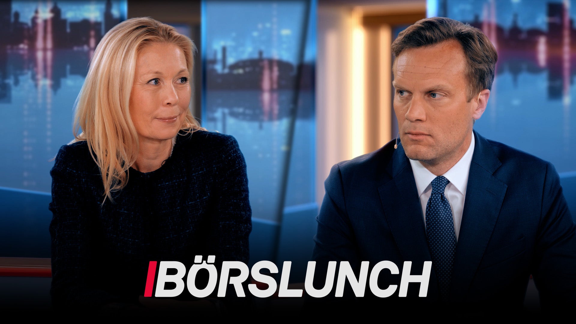 Två personer sitter vid ett skrivbord i en TV-studio med stadshorisont i bakgrunden. Texten Börslunch syns längst ned på skärmen.