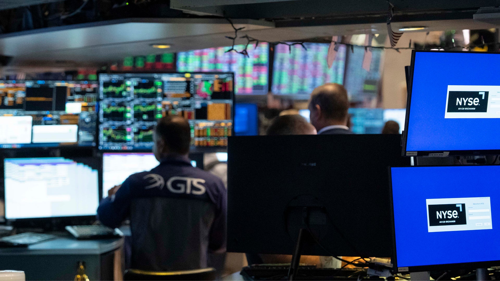 Börsmäklare arbetar vid New York Stock Exchange med flera dataskärmar som visar aktiekurser och marknadsdata.