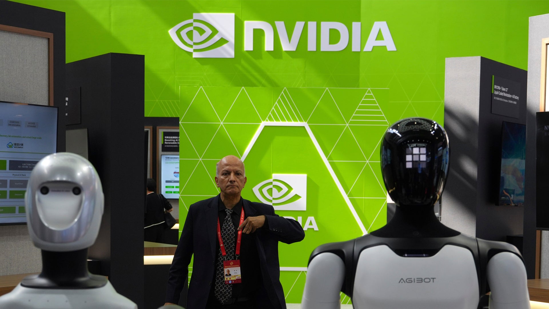 En man står mellan två humanoidrobottar framför en grön vägg med NVIDIA-logotypen på en utställning.