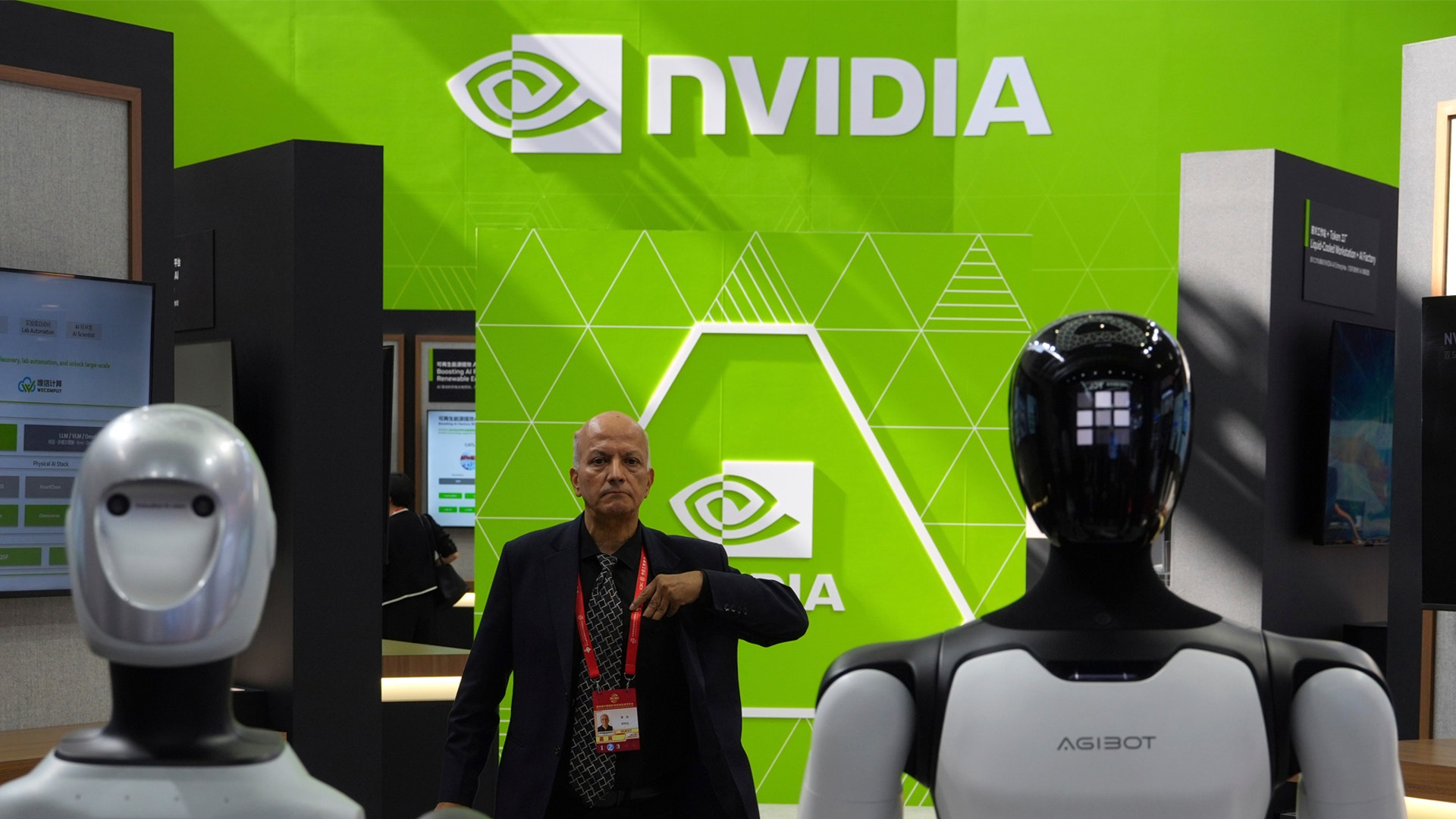 En man står mellan två humanoidrobottar framför en grön vägg med NVIDIA-logotypen på en utställning.