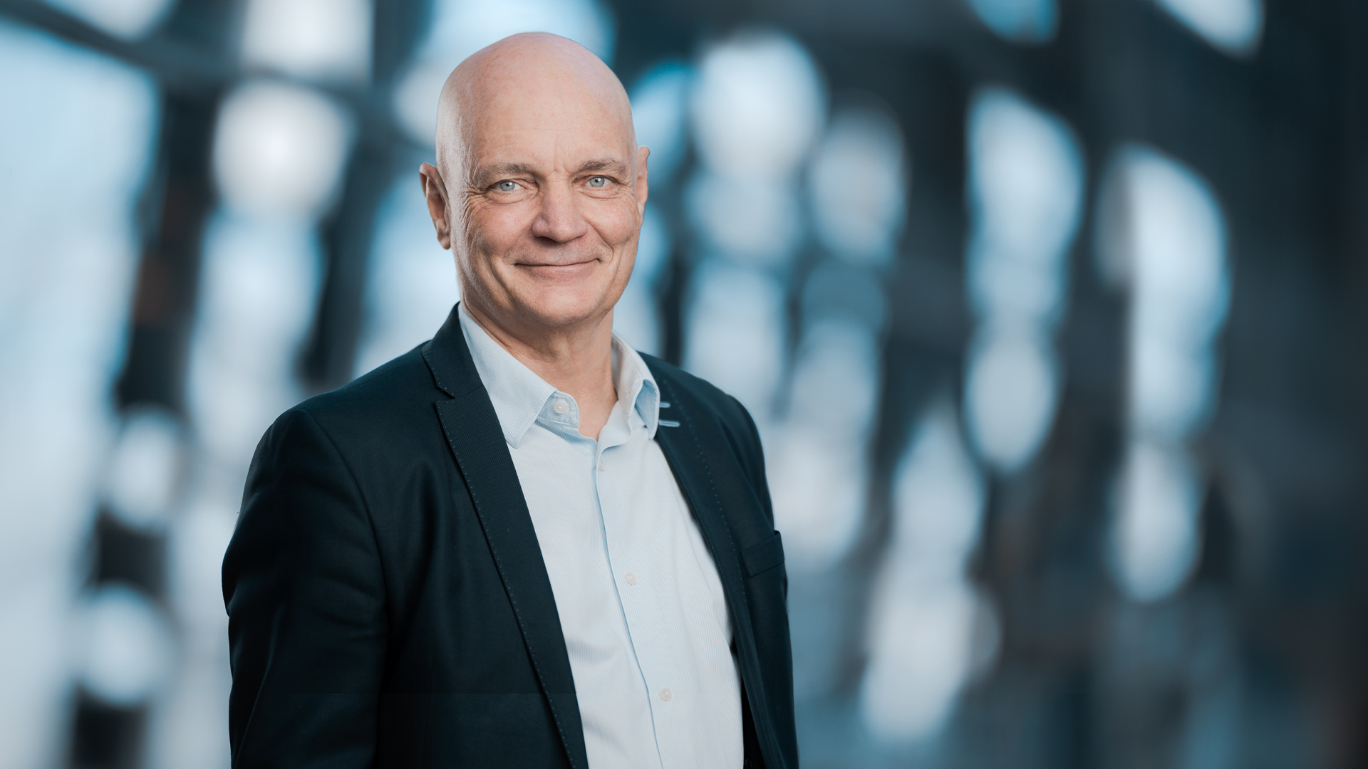 Porträttfoto av en man i mörkblå kavaj och ljusblå skjorta mot en suddig bakgrund.