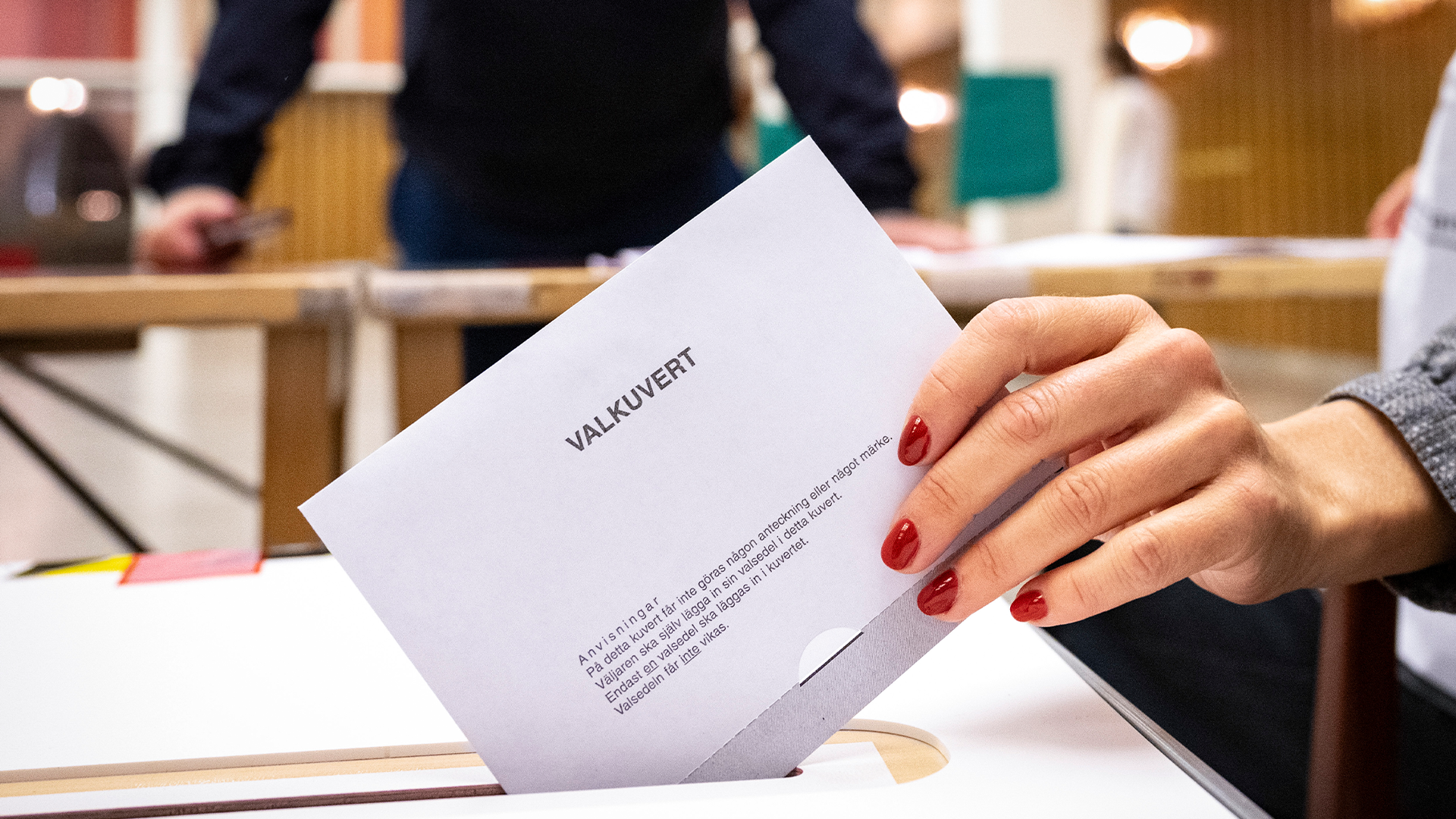 En hand lägger ett valkuvert i en valurna.