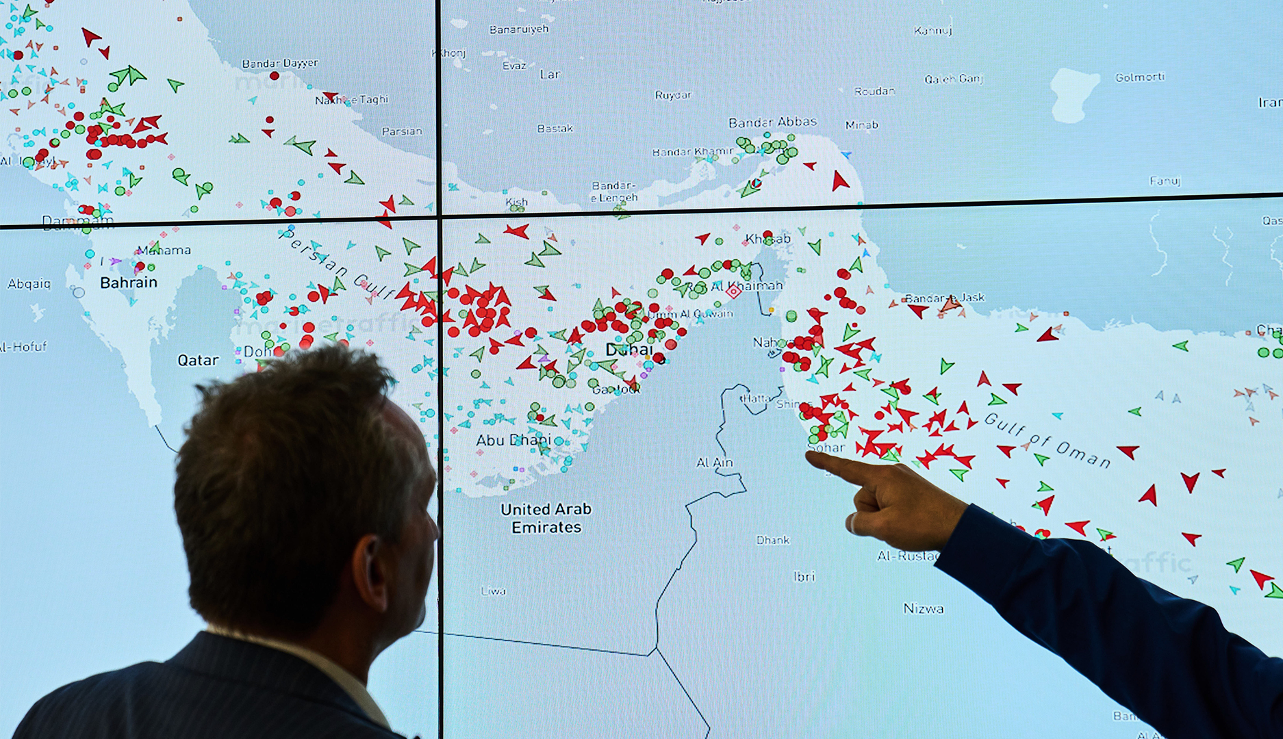 En person pekar på en digital världskarta med röda och gröna markeringar som visar olika geografiska platser.