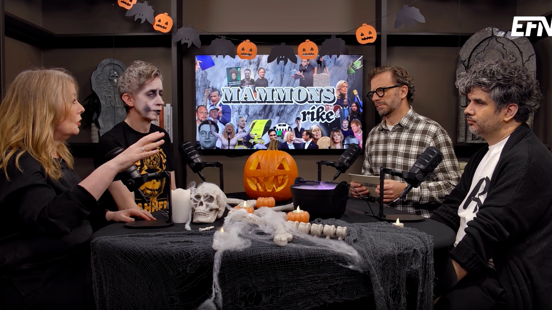 Fyra personer sitter vid ett halloweenpyntat bord i en studio och pratar i mikrofoner. Bakom dem visas en stor skärm med texten "Mammons rike".