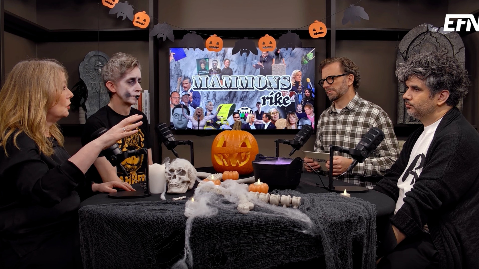 Fyra personer sitter vid ett halloweenpyntat bord i en studio och pratar i mikrofoner. Bakom dem visas en stor skärm med texten "Mammons rike".