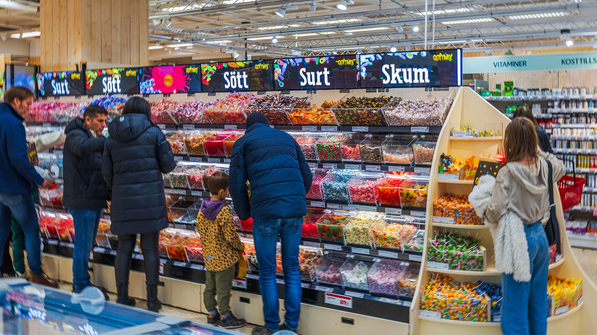 Kunder tittar på godis i en stor butiksdisplay med färgglada godisar och sötsaker.