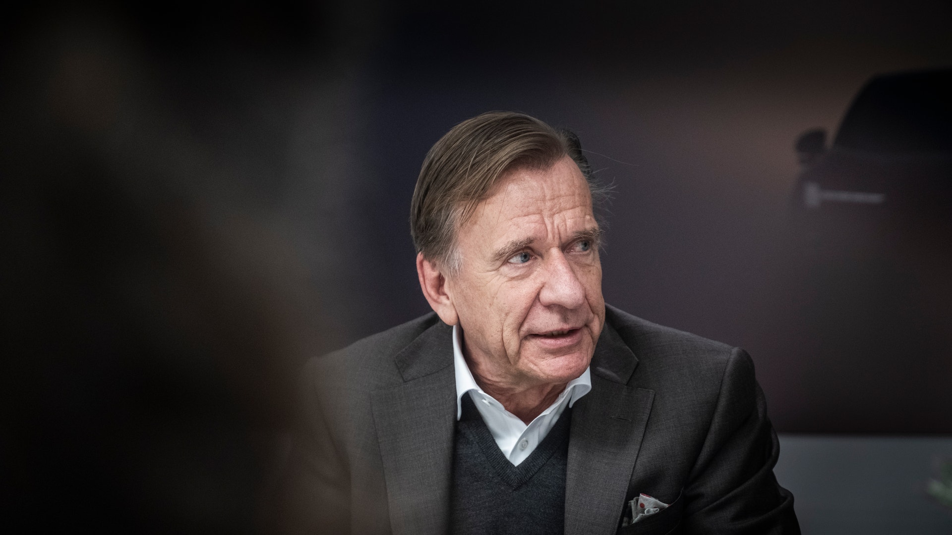Porträtt av en äldre man i mörk kostym och skjorta mot suddig bakgrund