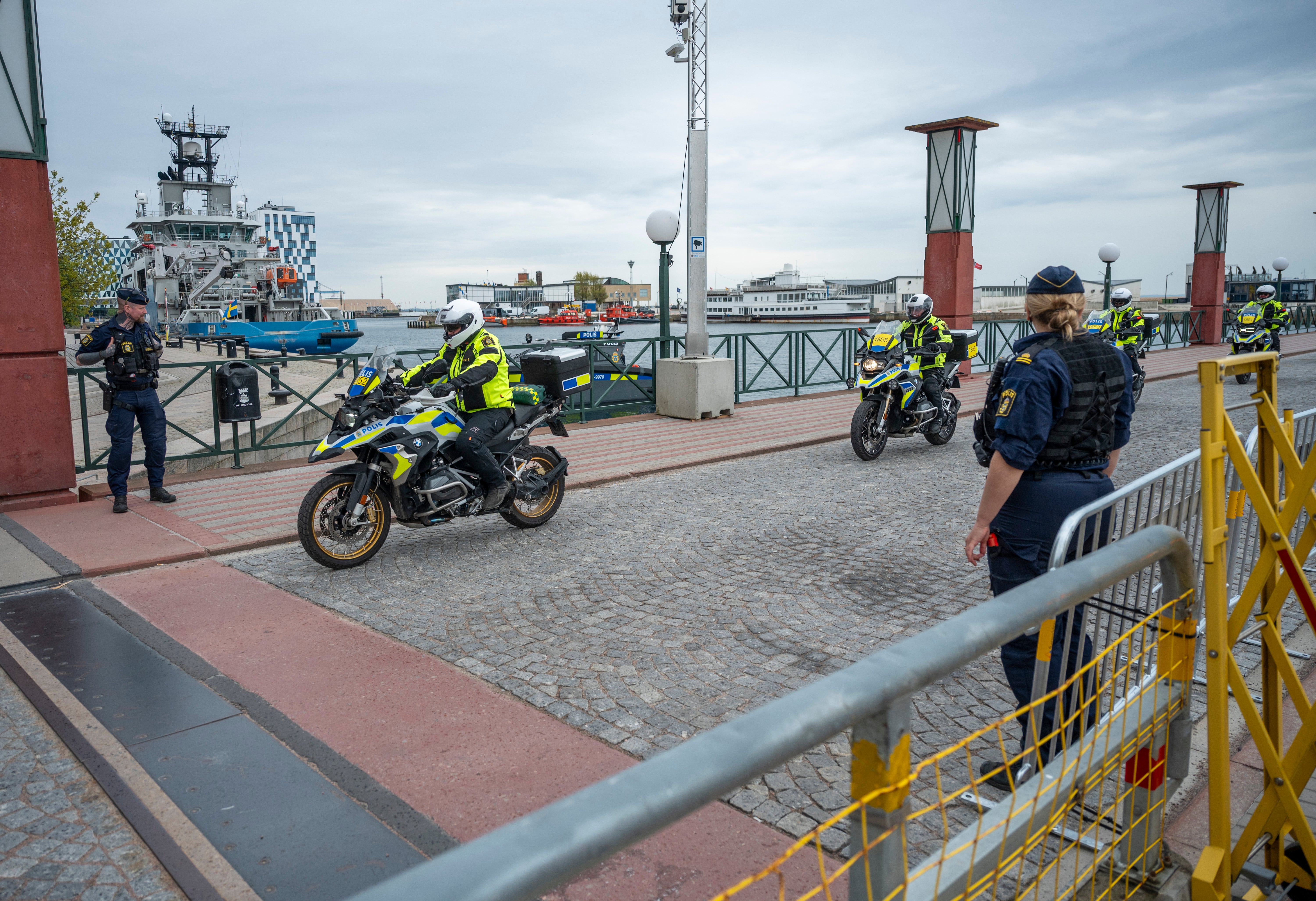 Polismotorcyklister i gul och blå utrustning utför en demonstration på en hamn. Båtar och hamnindustri syns i bakgrunden.
