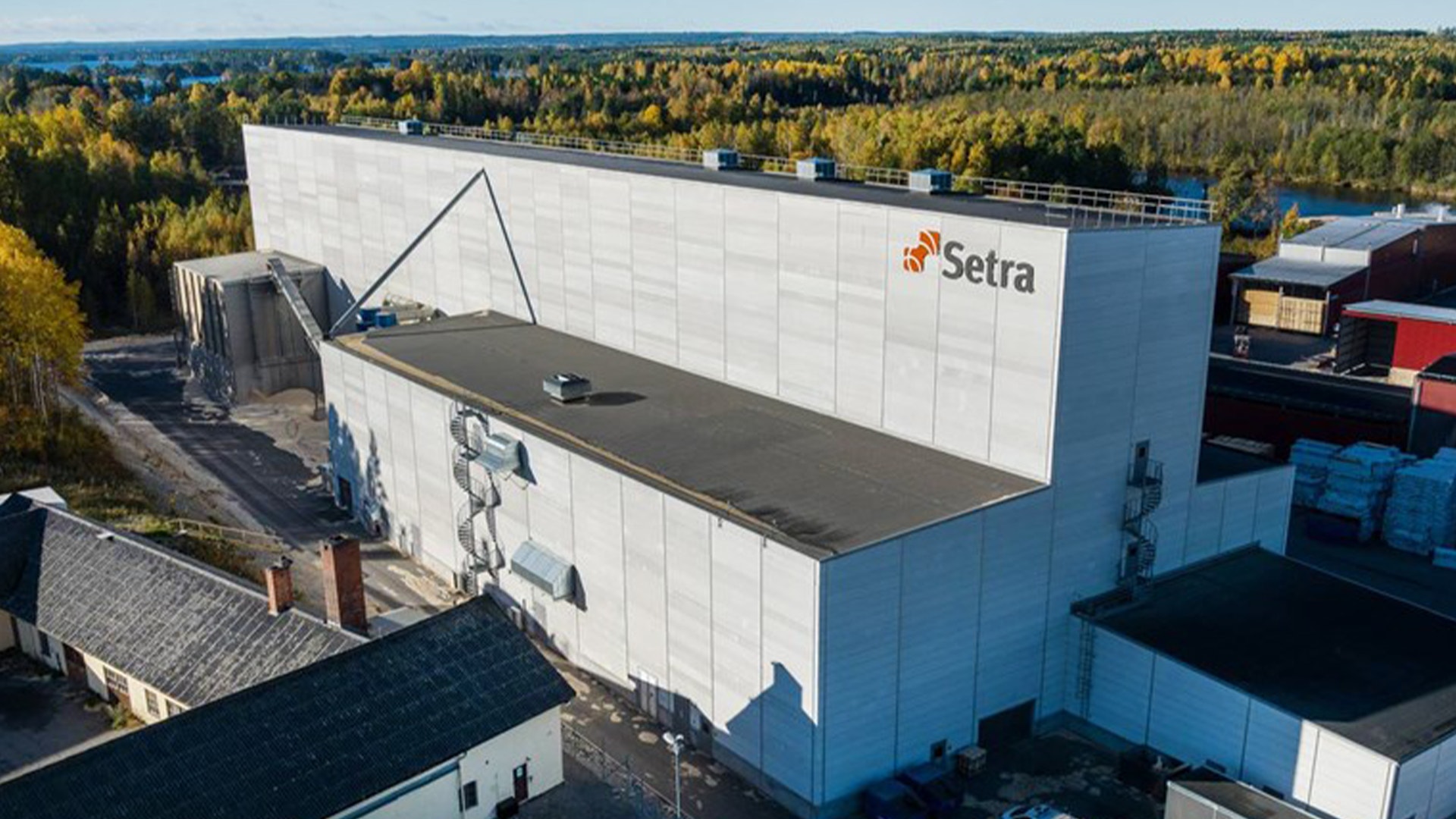 Setra-fabrik med vita och blå byggnader omgivna av skog