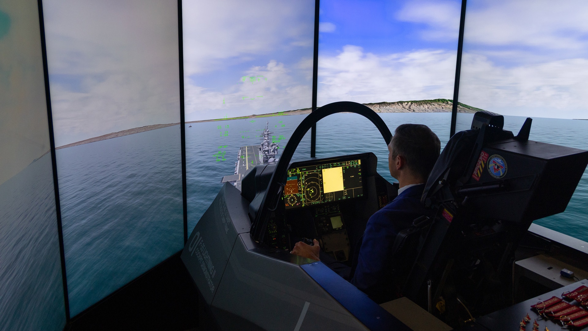 Pilot i en flygsimulatorkabinär med ratt och instrumentpanel, med en stor skärmvisning av havet och himlen.