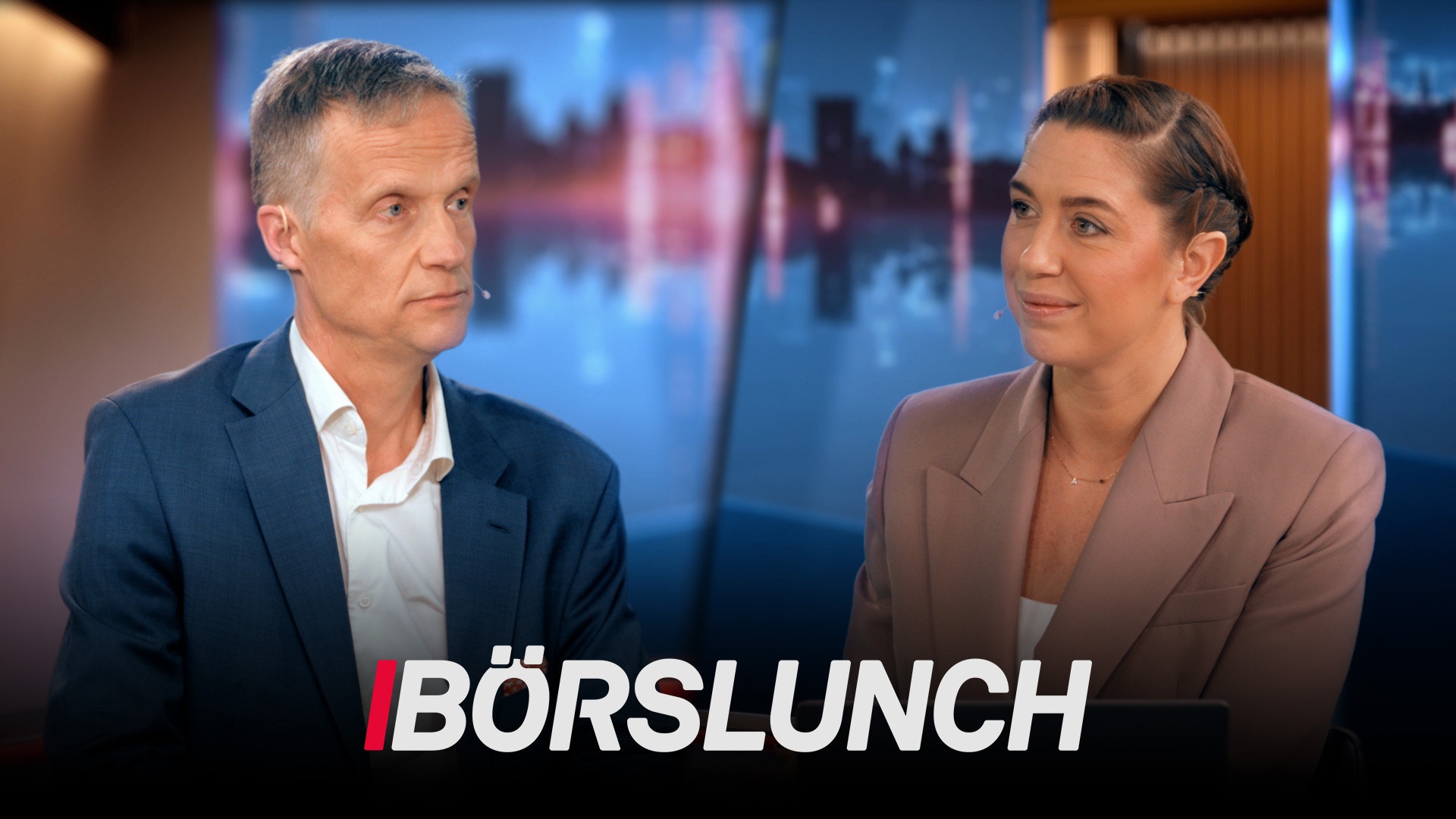 Två affärspersoner i samtal framför en stadshorisont. Text "BÖRSLUNCH" visas längst ned.