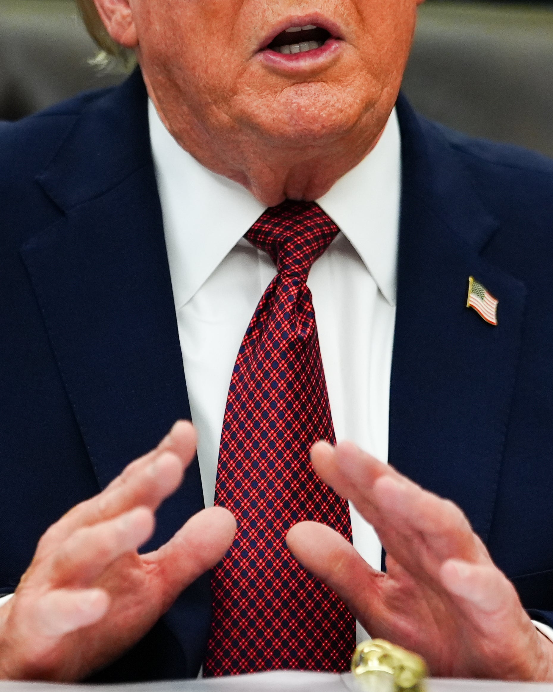 Man i mörkblå kostym och röd slips gestikulerar medan han talar.