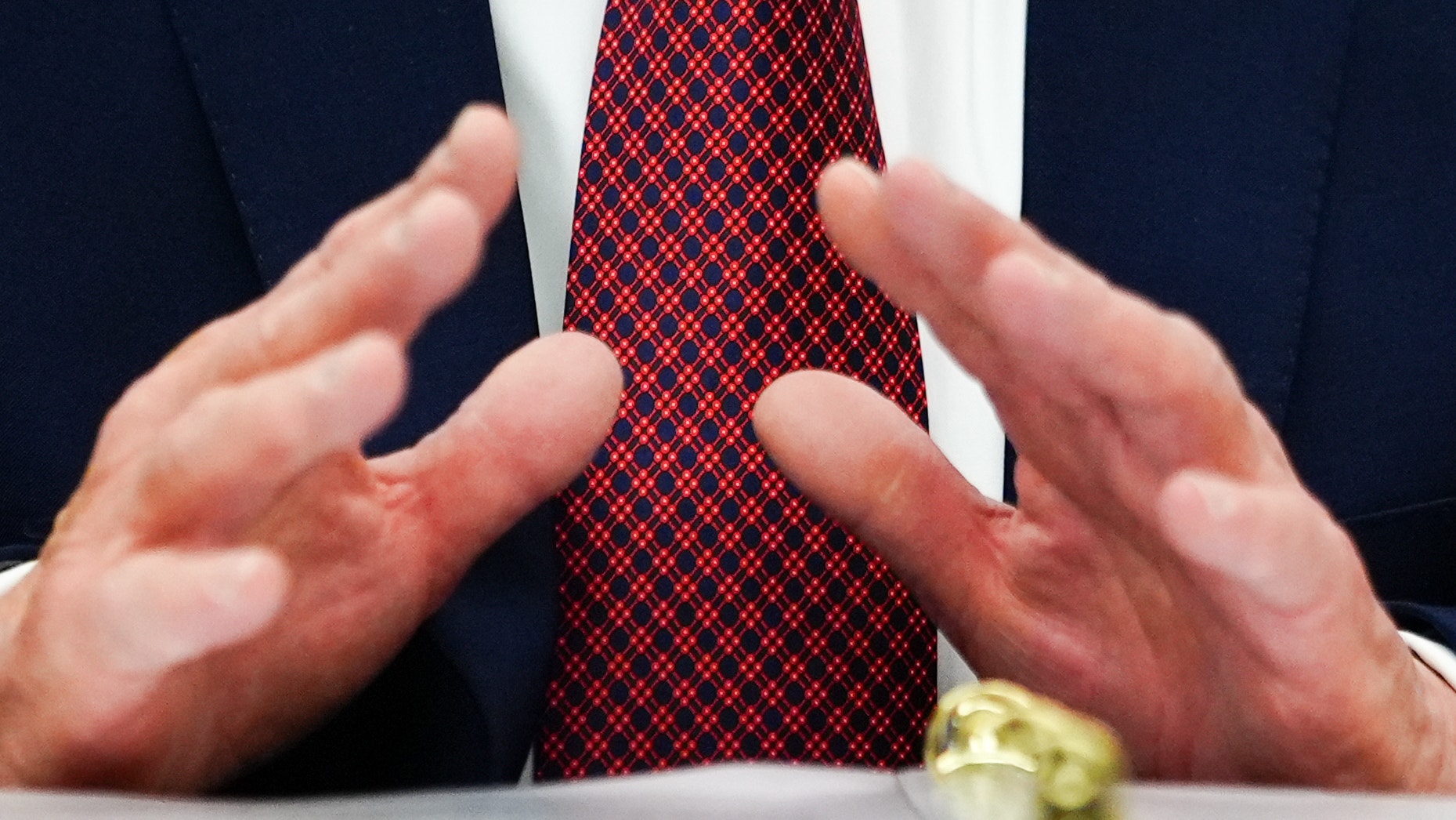 Man i mörkblå kostym och röd slips gestikulerar medan han talar.