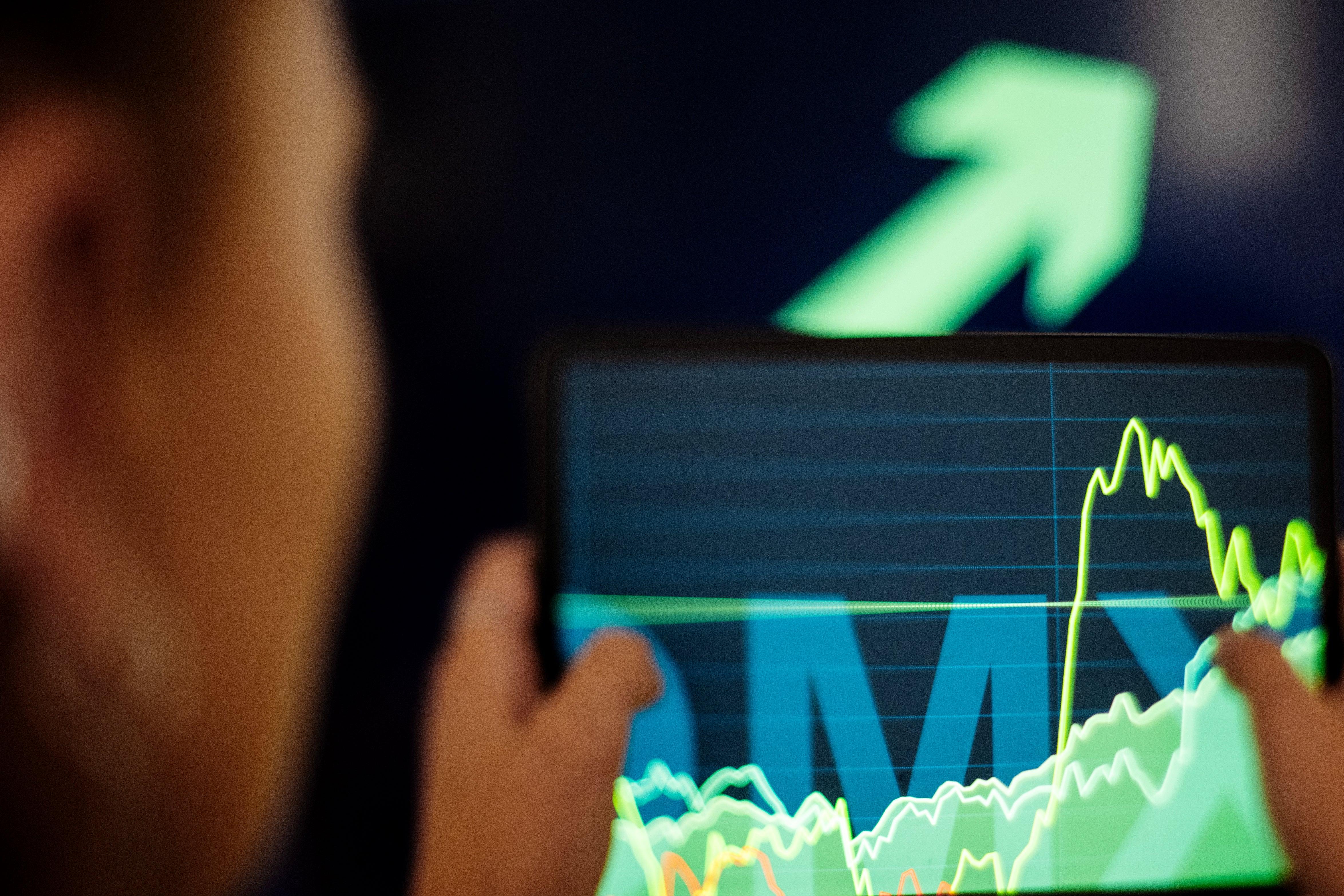 Person tittar på en datorskärm med finansiella grafer och diagram som visar aktiekurser och marknadstrender i grönt och gult.