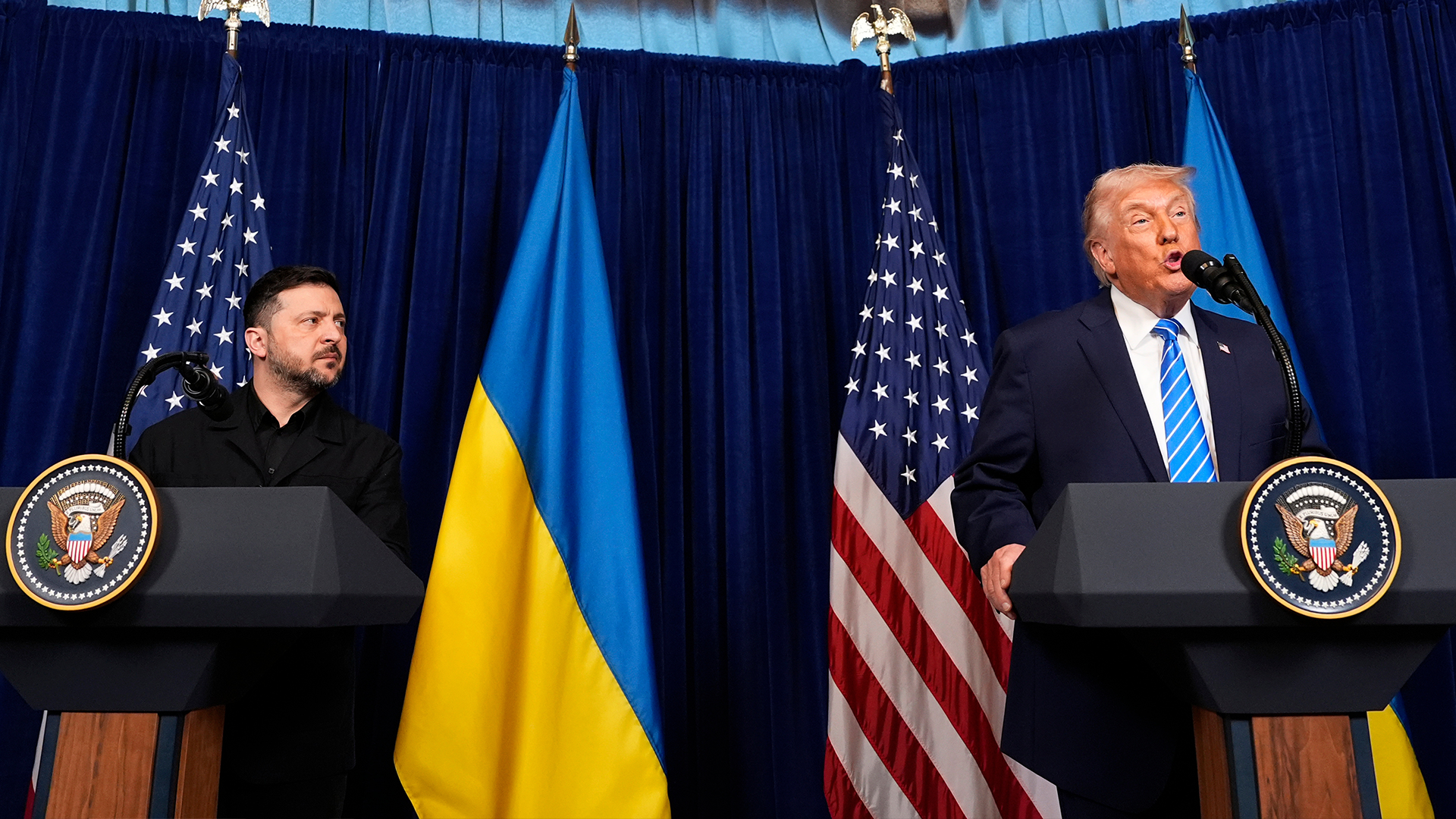 Två män vid talarstolar under amerikanska och ukrainska flaggor under en presskonferens.