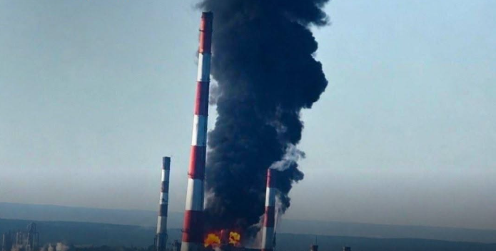 Industriell skorsten med röd och vit färgning som släpper ut tjock svart rök från en brand.