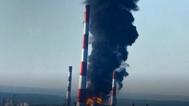 Industriell skorsten med röd och vit färgning som släpper ut tjock svart rök från en brand.