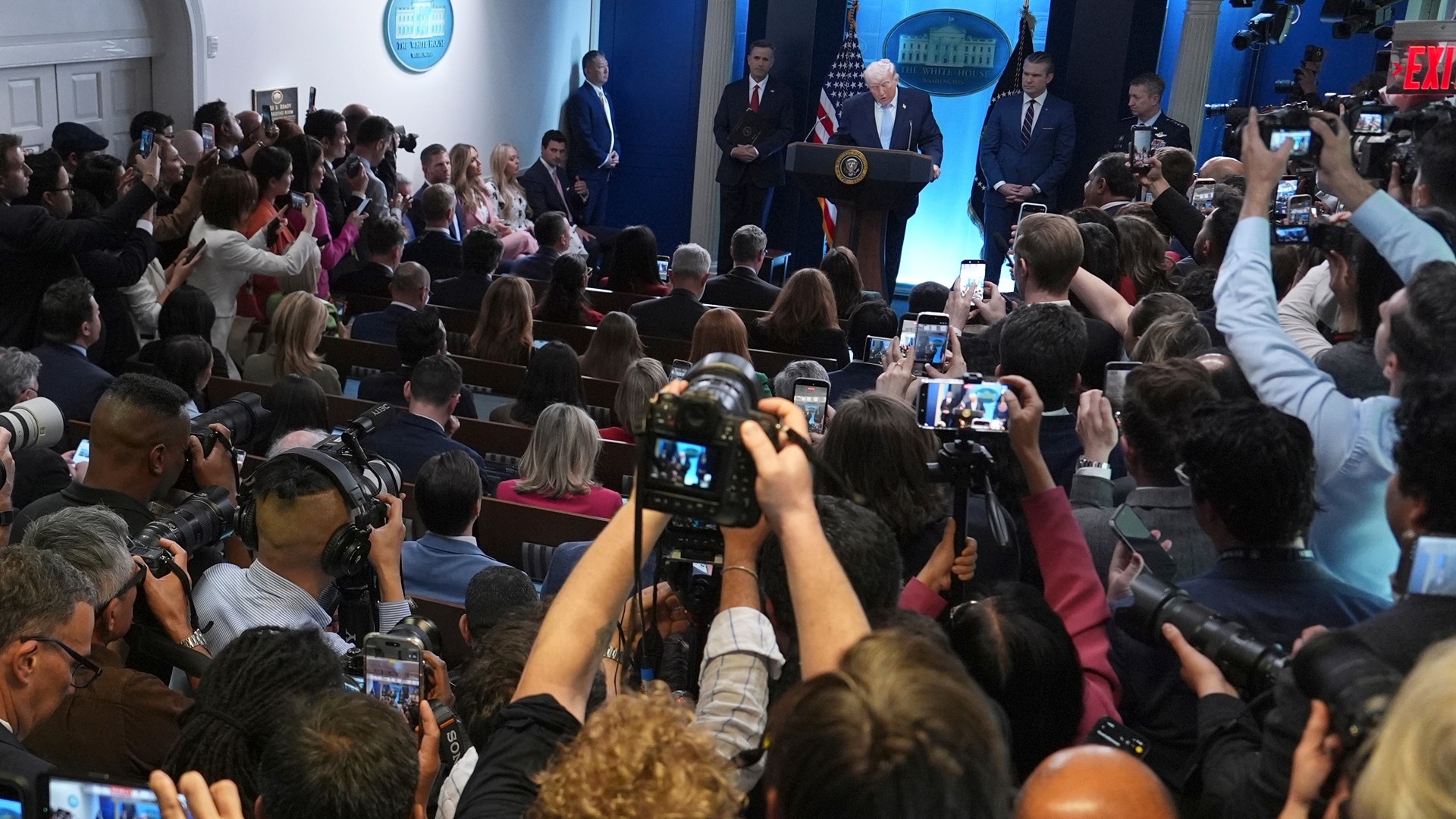 En presskonferens med talare på en podium omgivna av journalister och fotografer