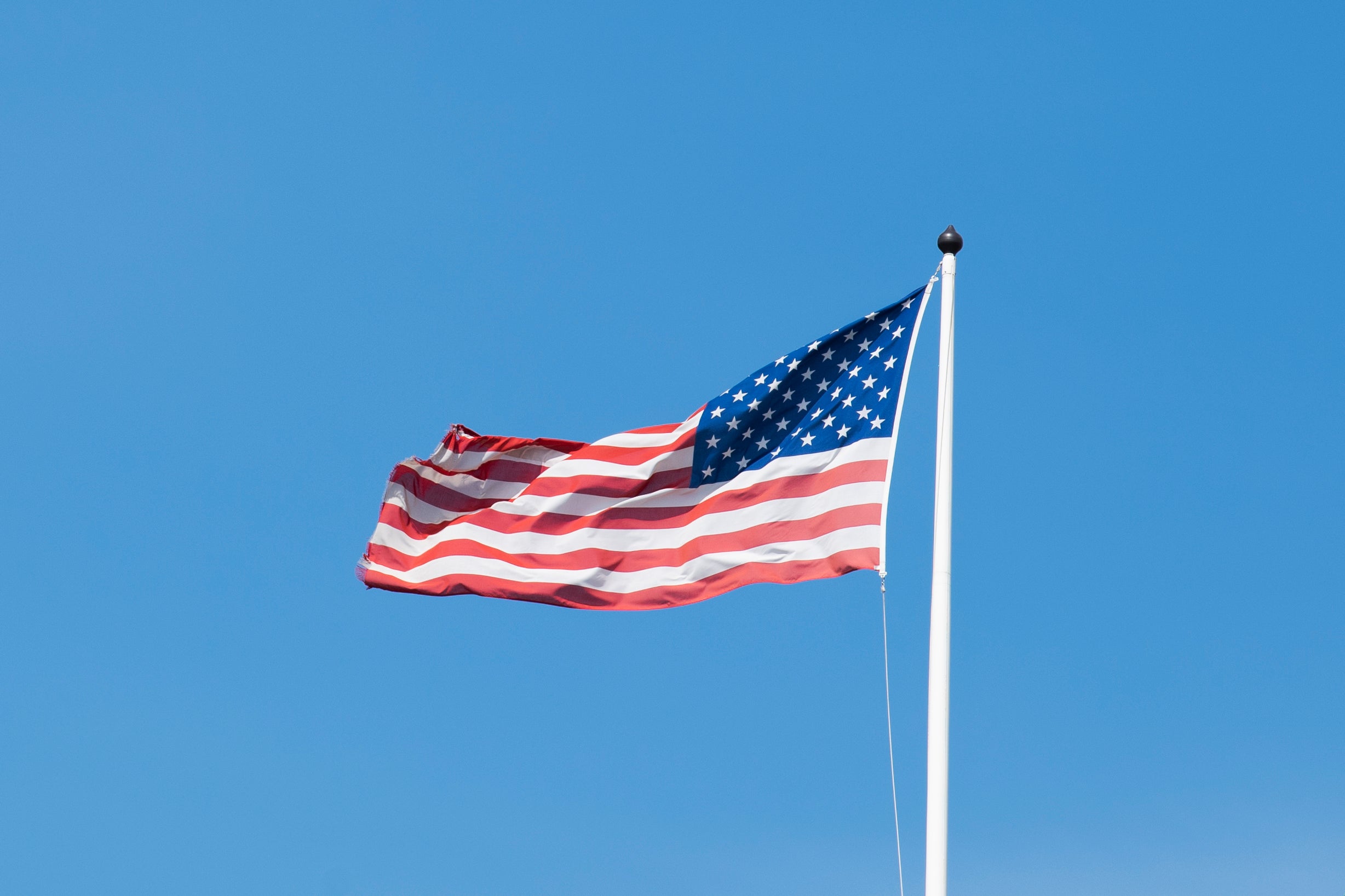 Amerikansk flagga som vajar på en vit flaggstång mot en klar blå himmel.
