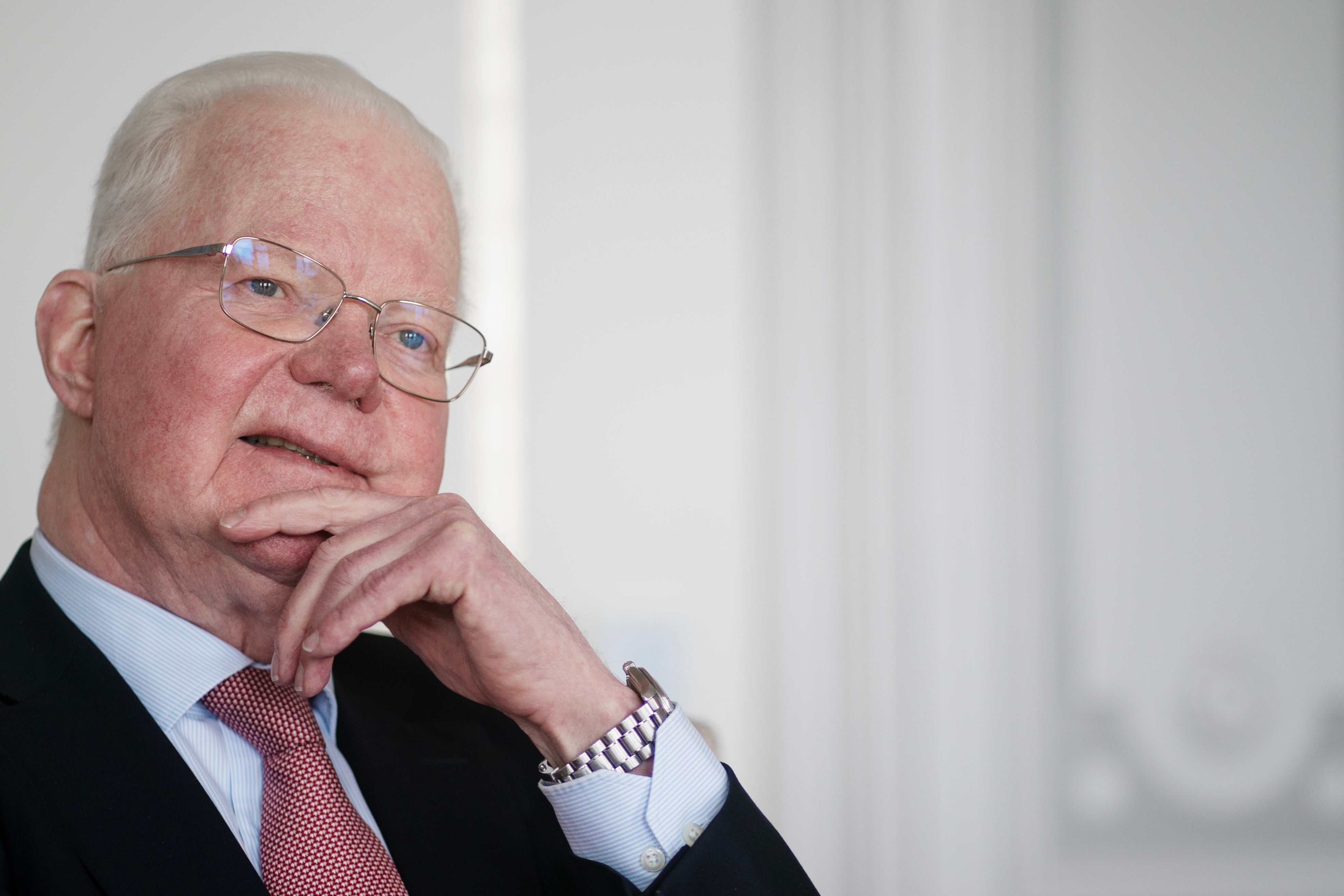 Porträtt av en äldre man med glasögon som sitter i en eftertänksam pose med handen mot ansiktet.