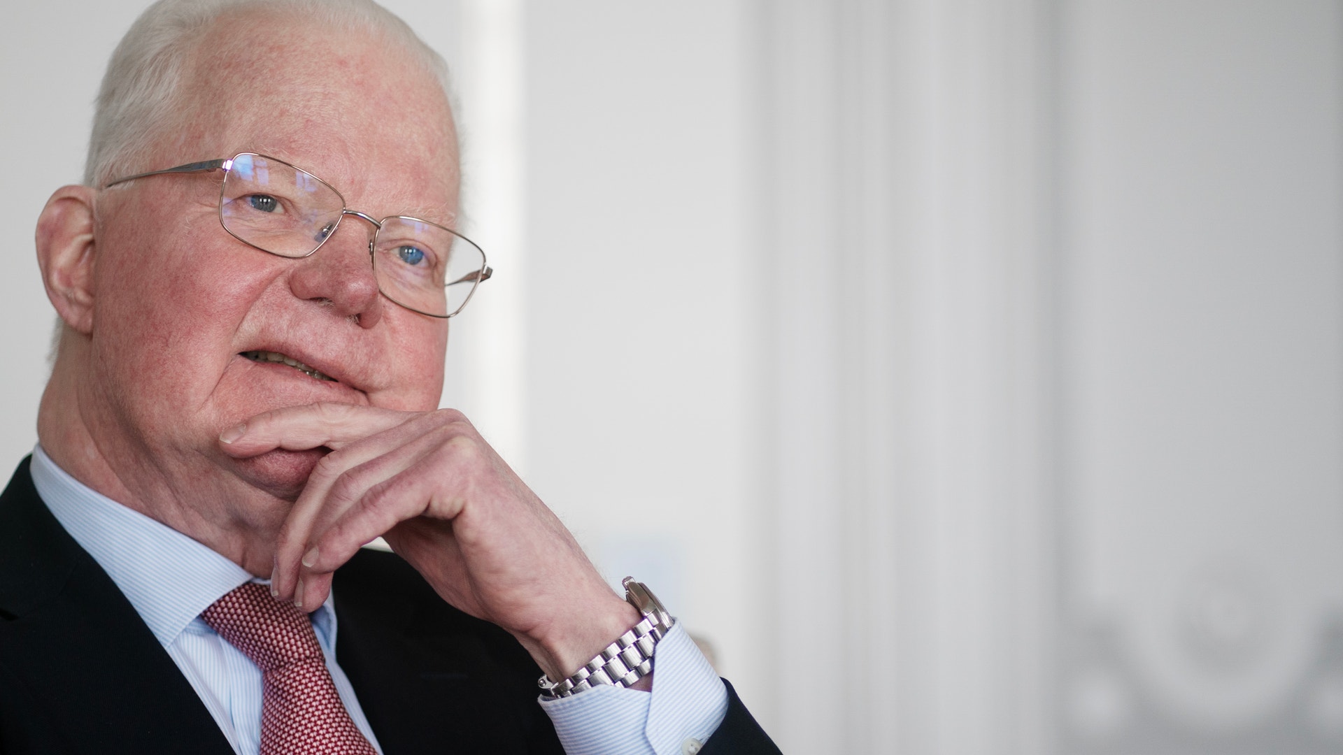 Porträtt av en äldre man med glasögon som sitter i en eftertänksam pose med handen mot ansiktet.
