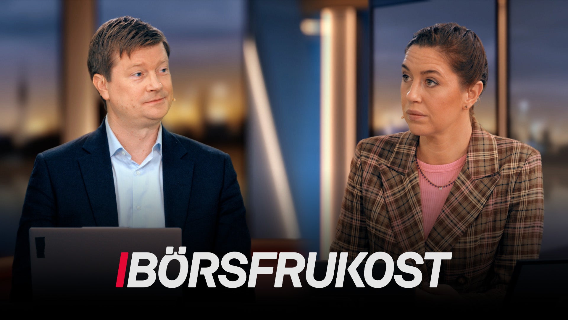 Två personer i studiomiljö med stadsutsikt i bakgrunden.