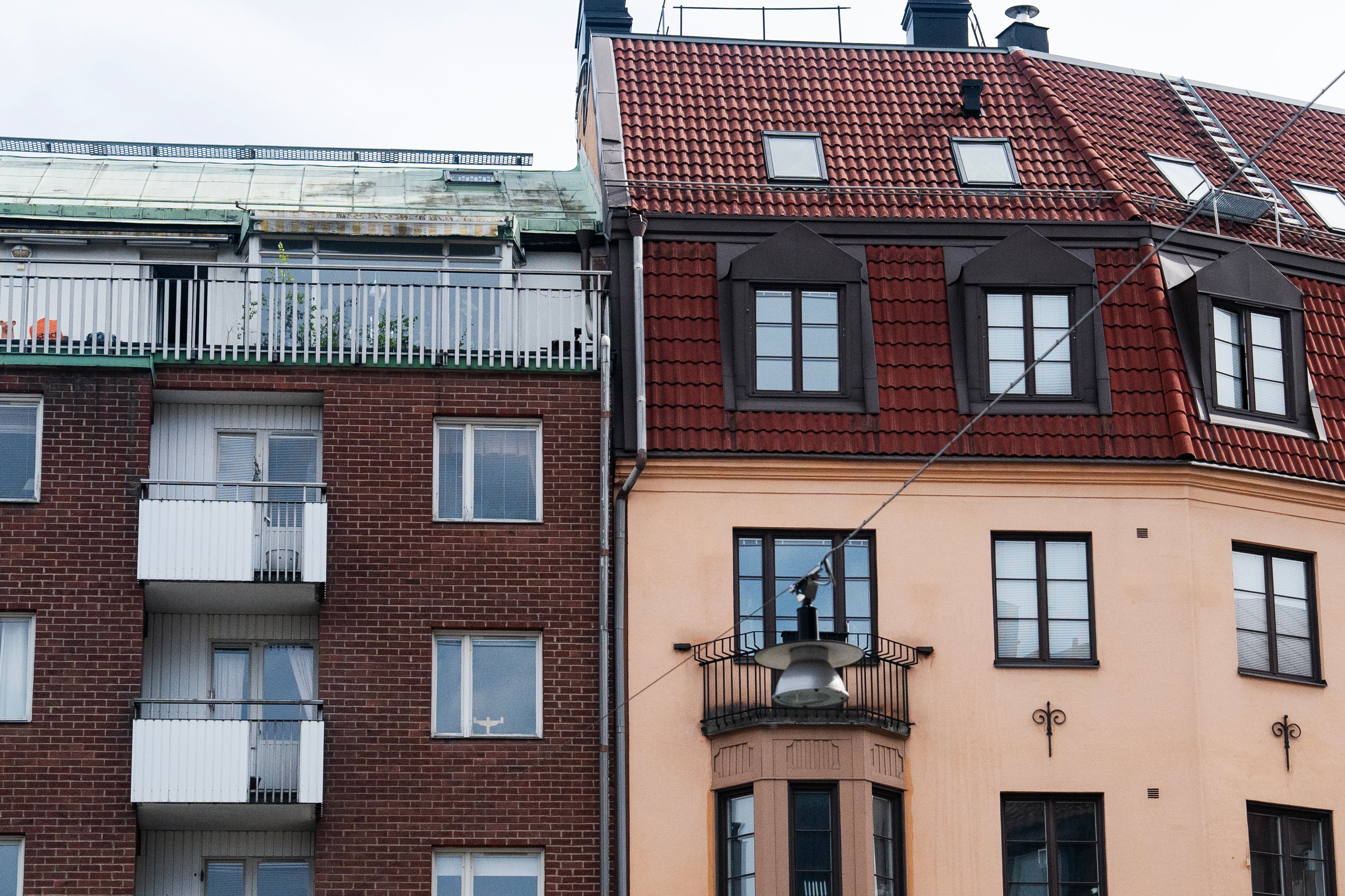 Två intilliggande bostadshus med olika fasader. Till vänster ett rödbrunt tegelshus med vita balkonger, till höger ett gult hus med rött tegeltaket och svarta fönster.